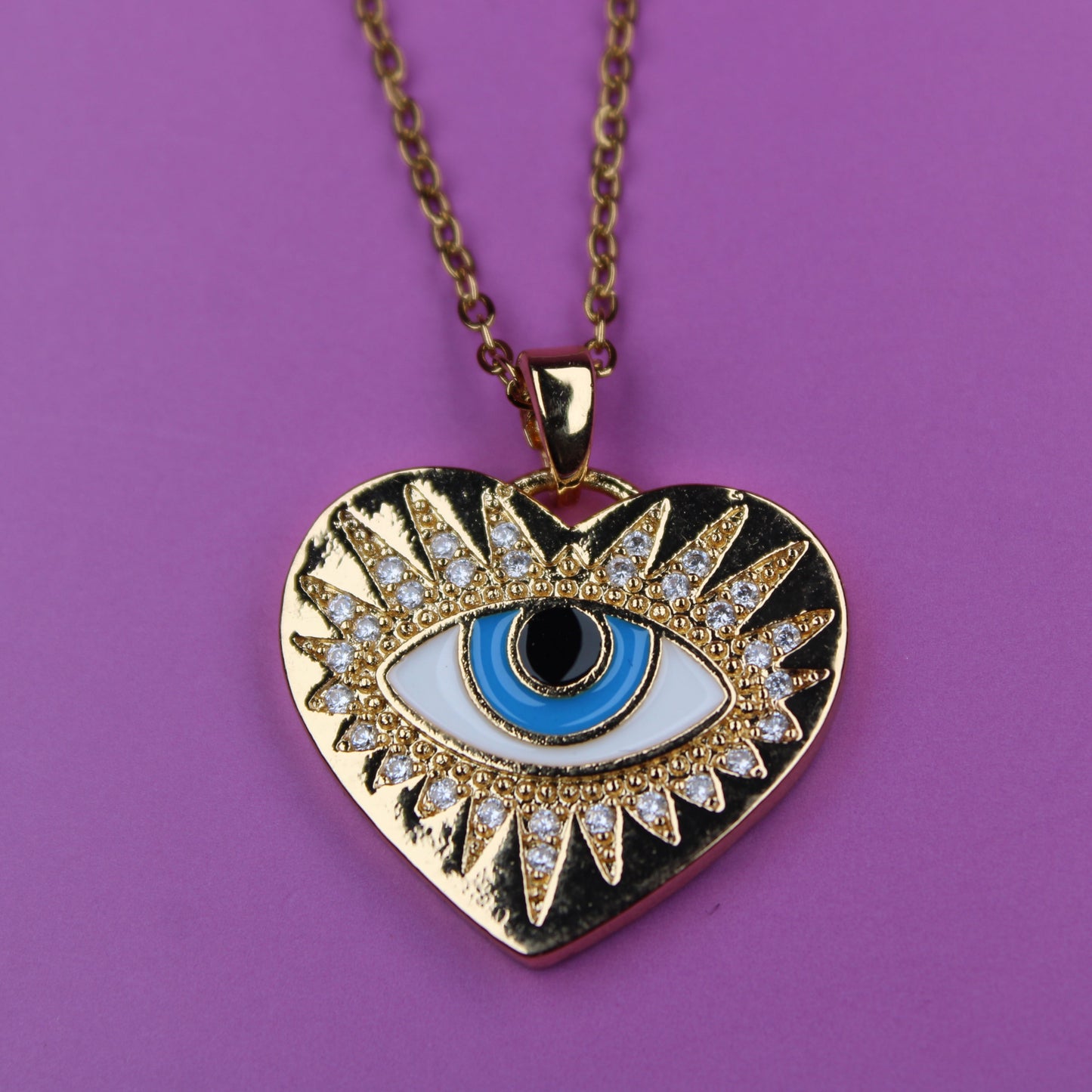Gold heart-shaped necklace with an eye design on a purple background