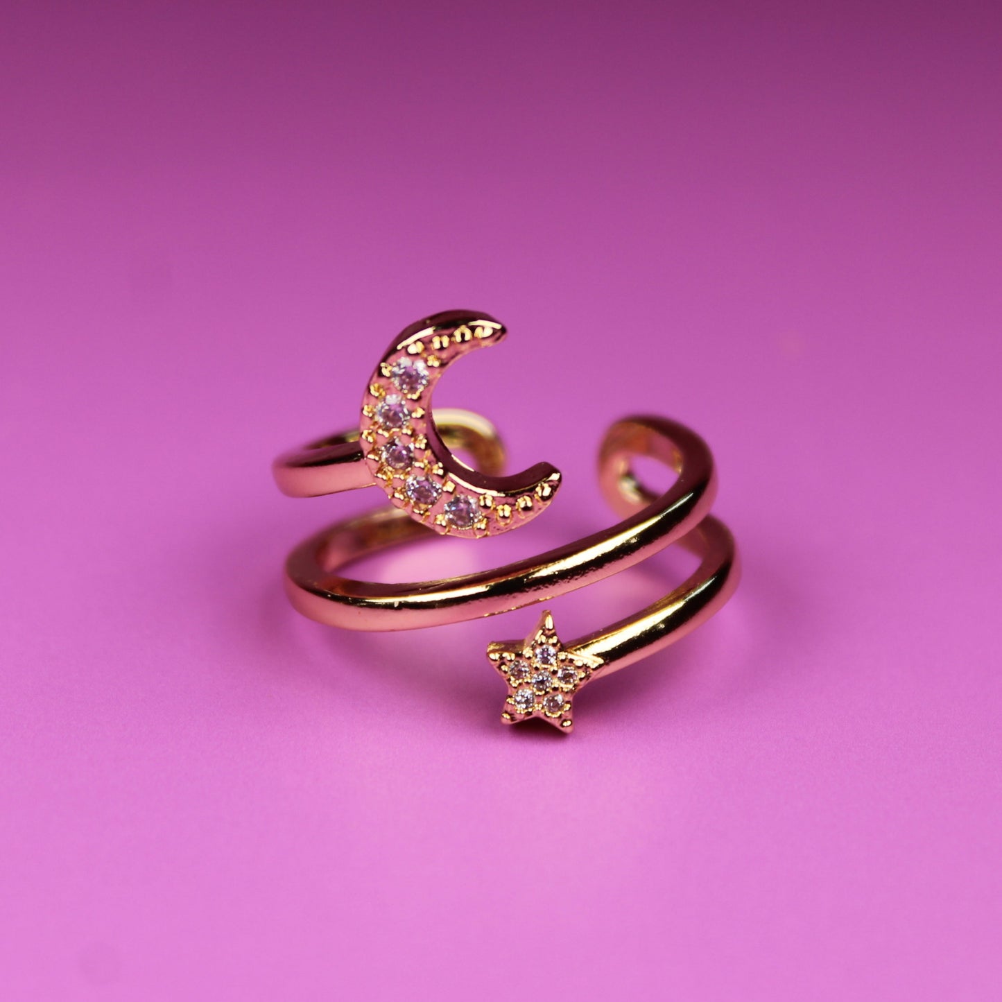 Rose gold open ring with moon and star designs on a pink background
