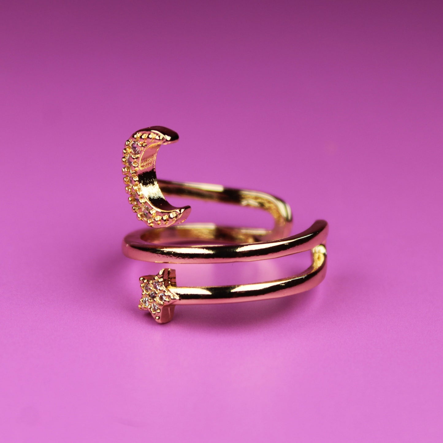 Gold ring with moon and star designs on a pink background