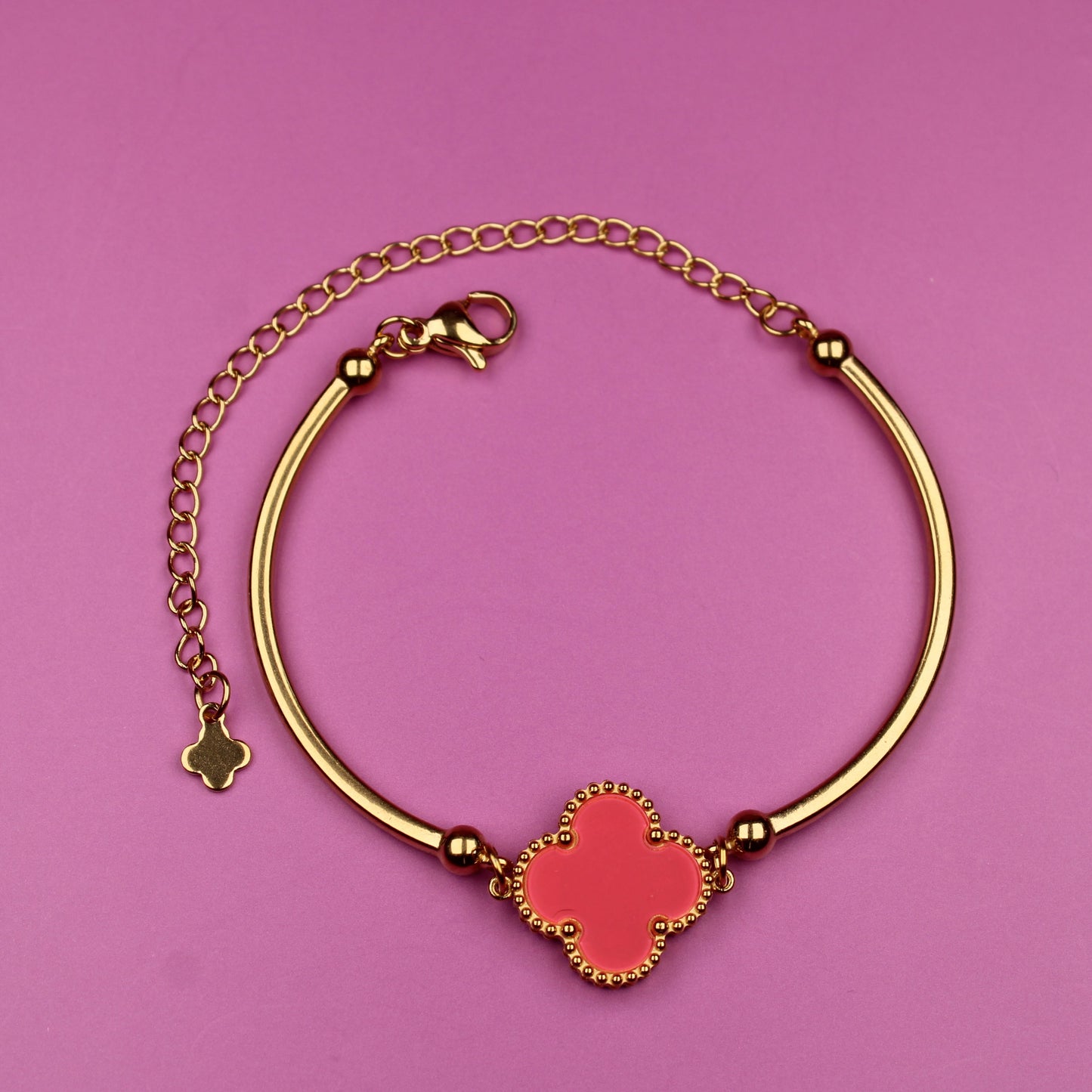 Gold bracelet with a red clover charm on a pink background