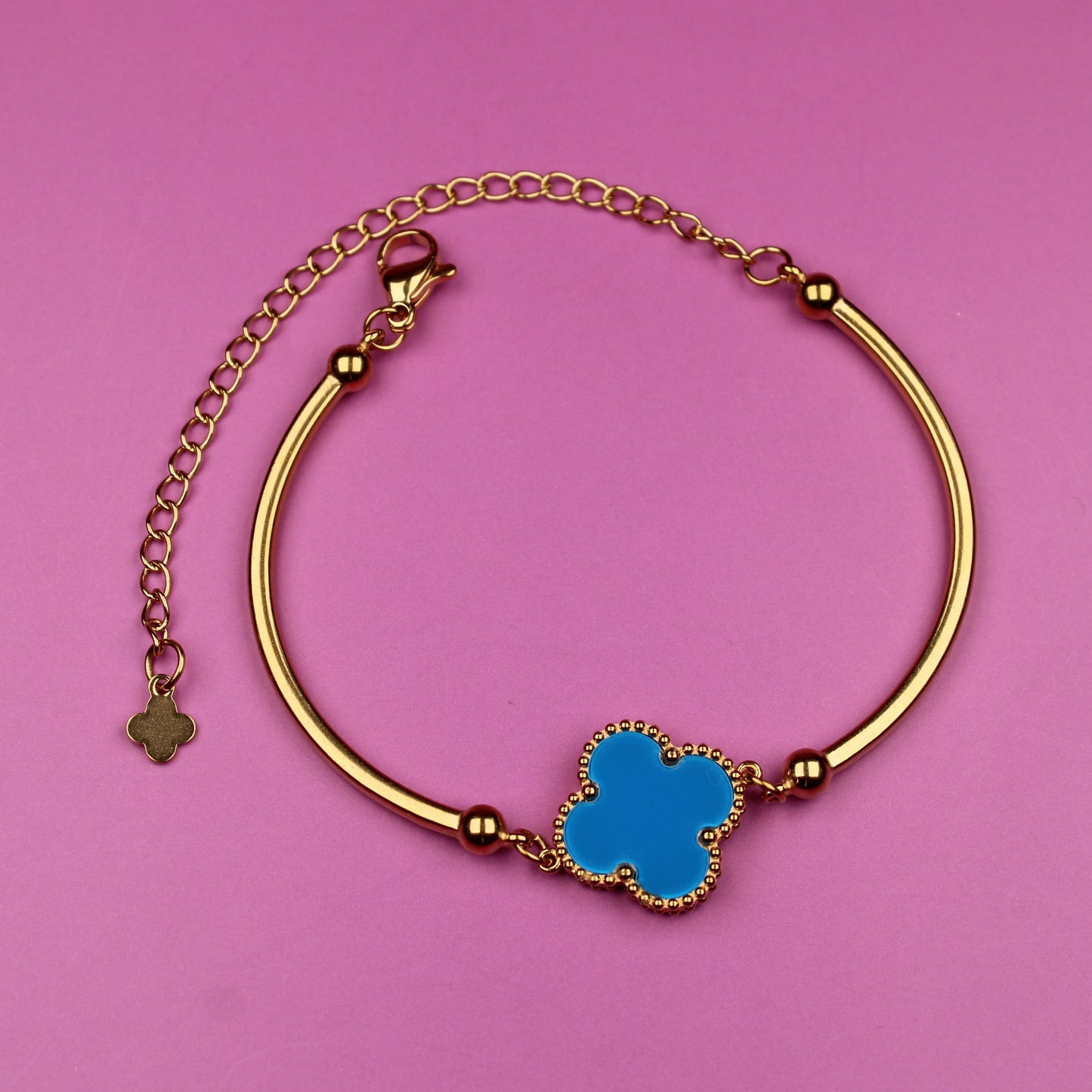 Gold bracelet with a blue clover charm on a pink background