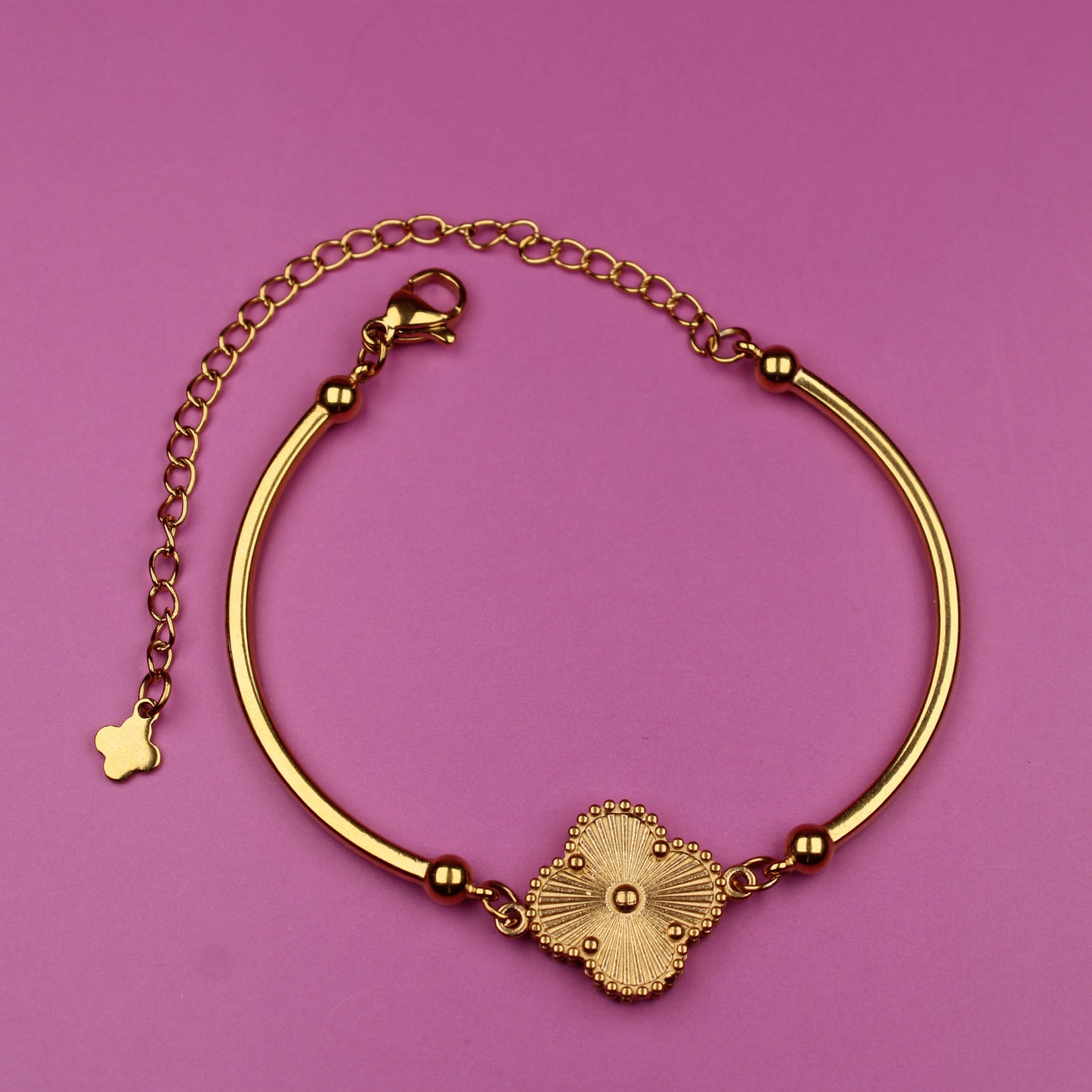 Gold bracelet with a decorative clasp on a pink background