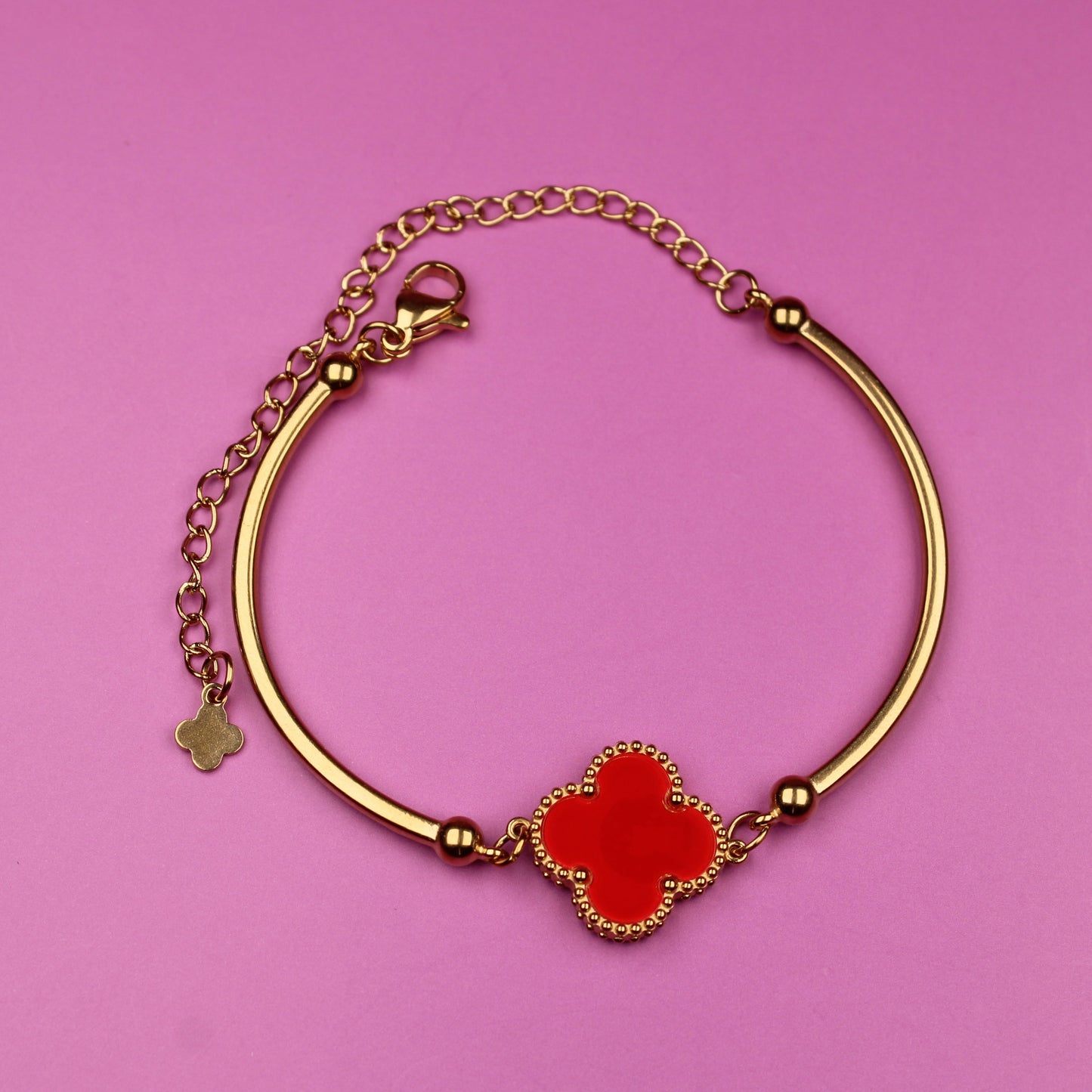 Gold bracelet with a red clover charm on a pink background