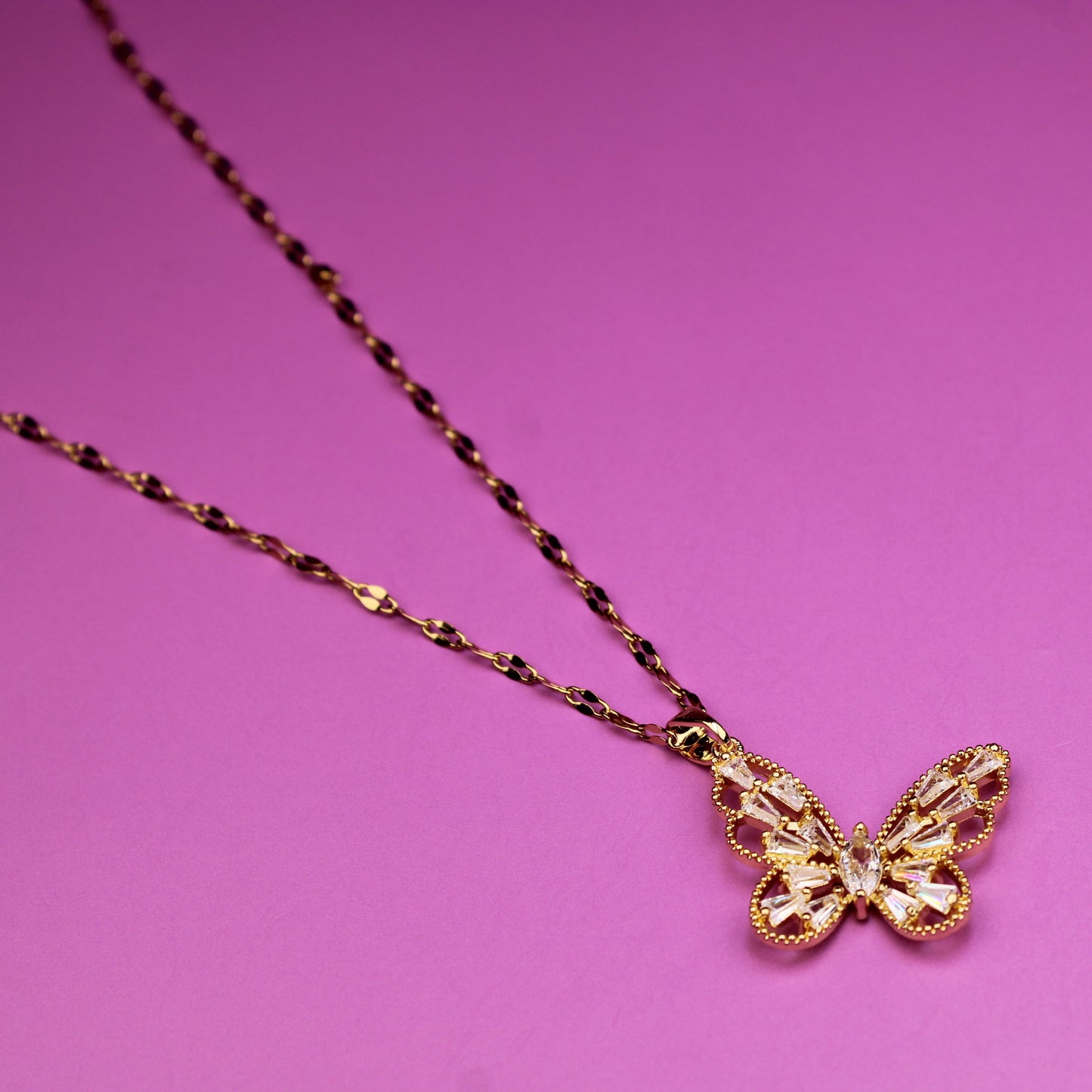 Gold butterfly pendant necklace on a pink background