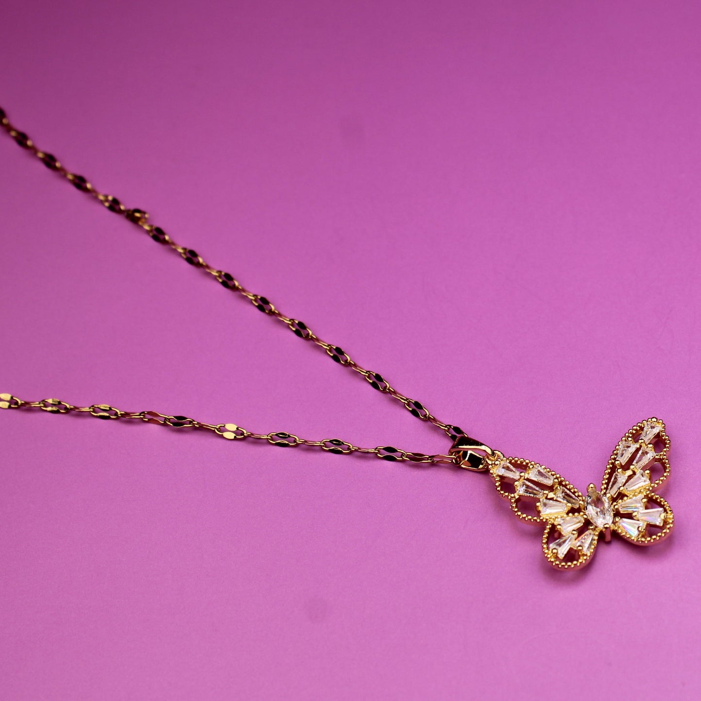 Gold butterfly pendant necklace on a pink background