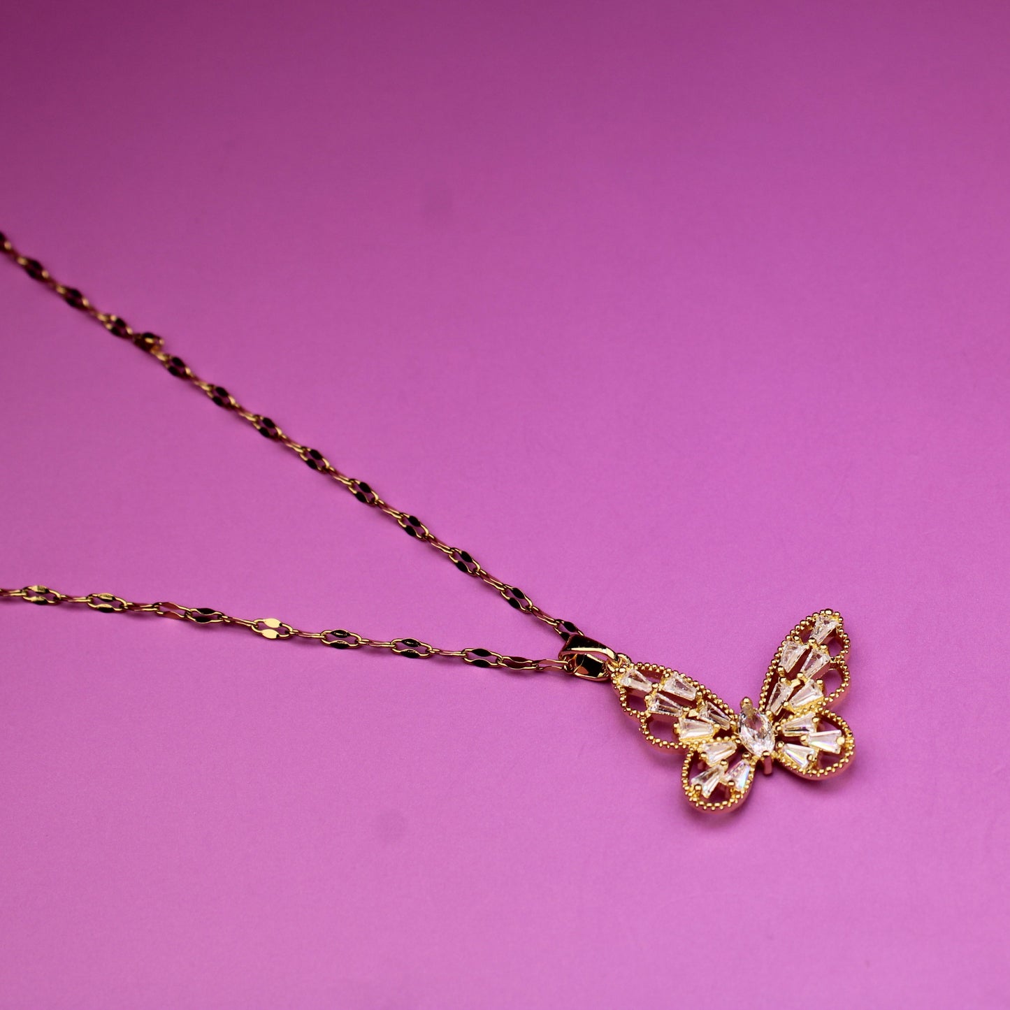 Gold butterfly necklace on a pink background