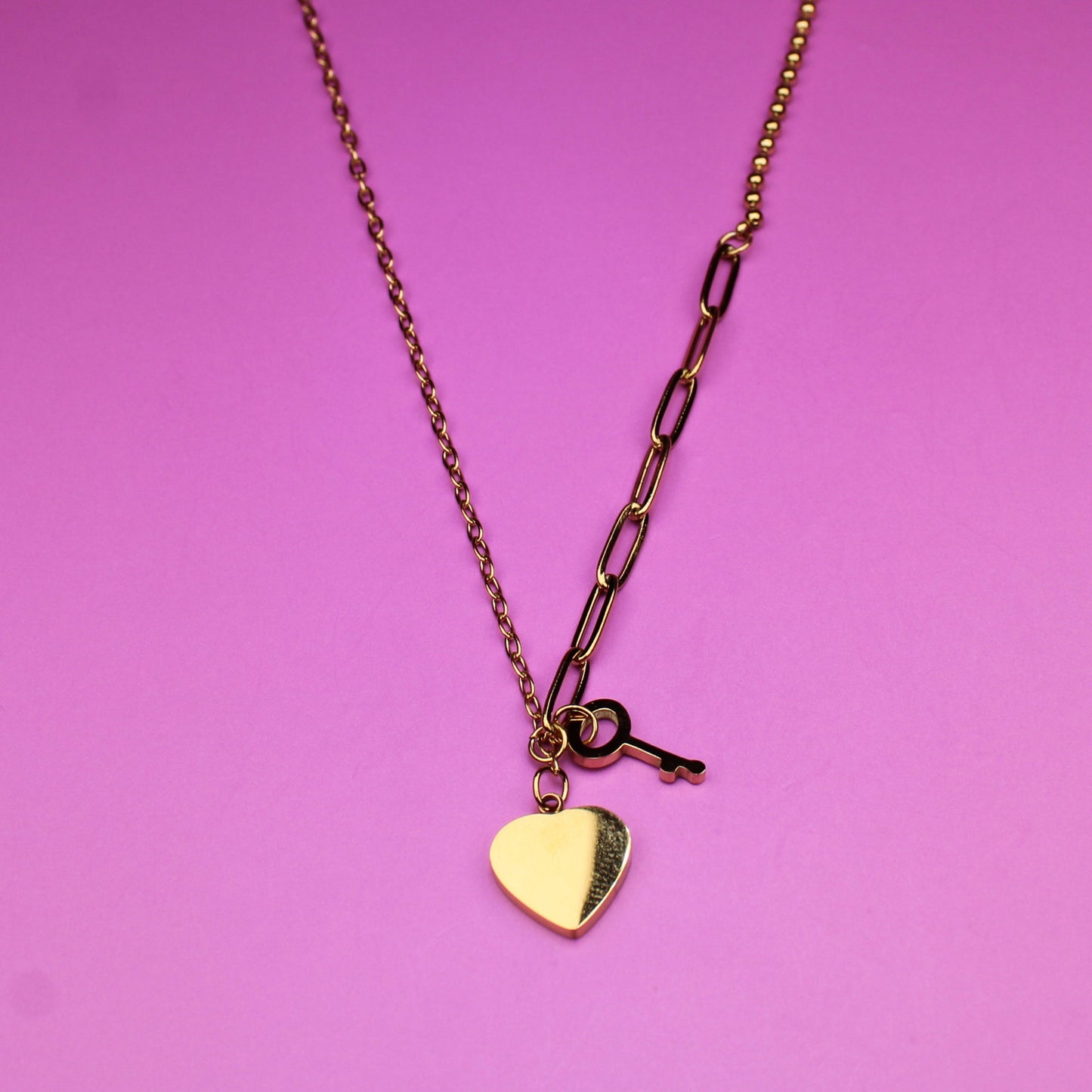 Gold necklace with a heart pendant on a pink background