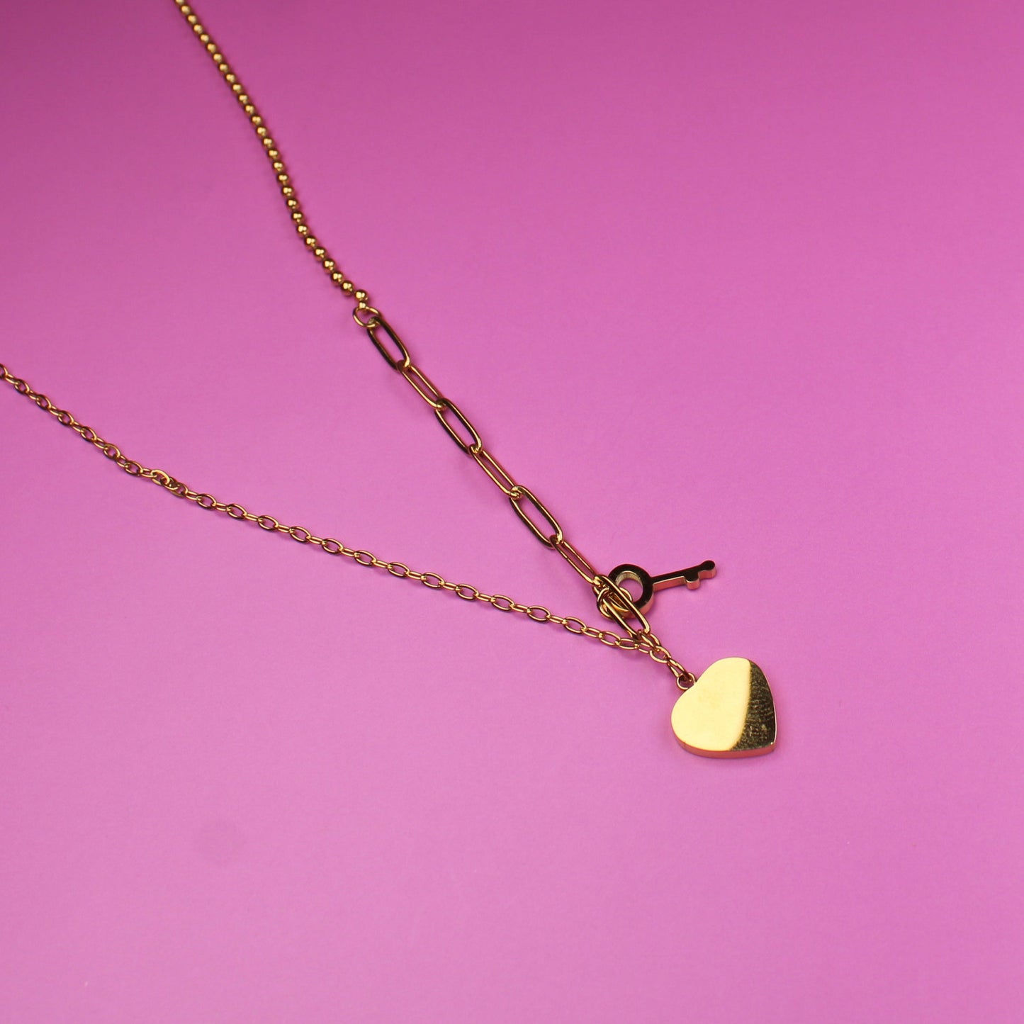 Gold necklace with a heart pendant on a pink surface