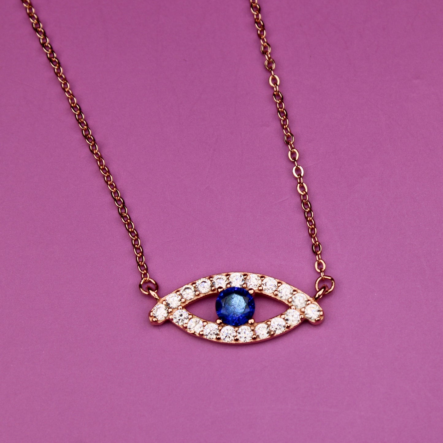 Necklace with eye-shaped pendant featuring a blue gemstone on a pink background