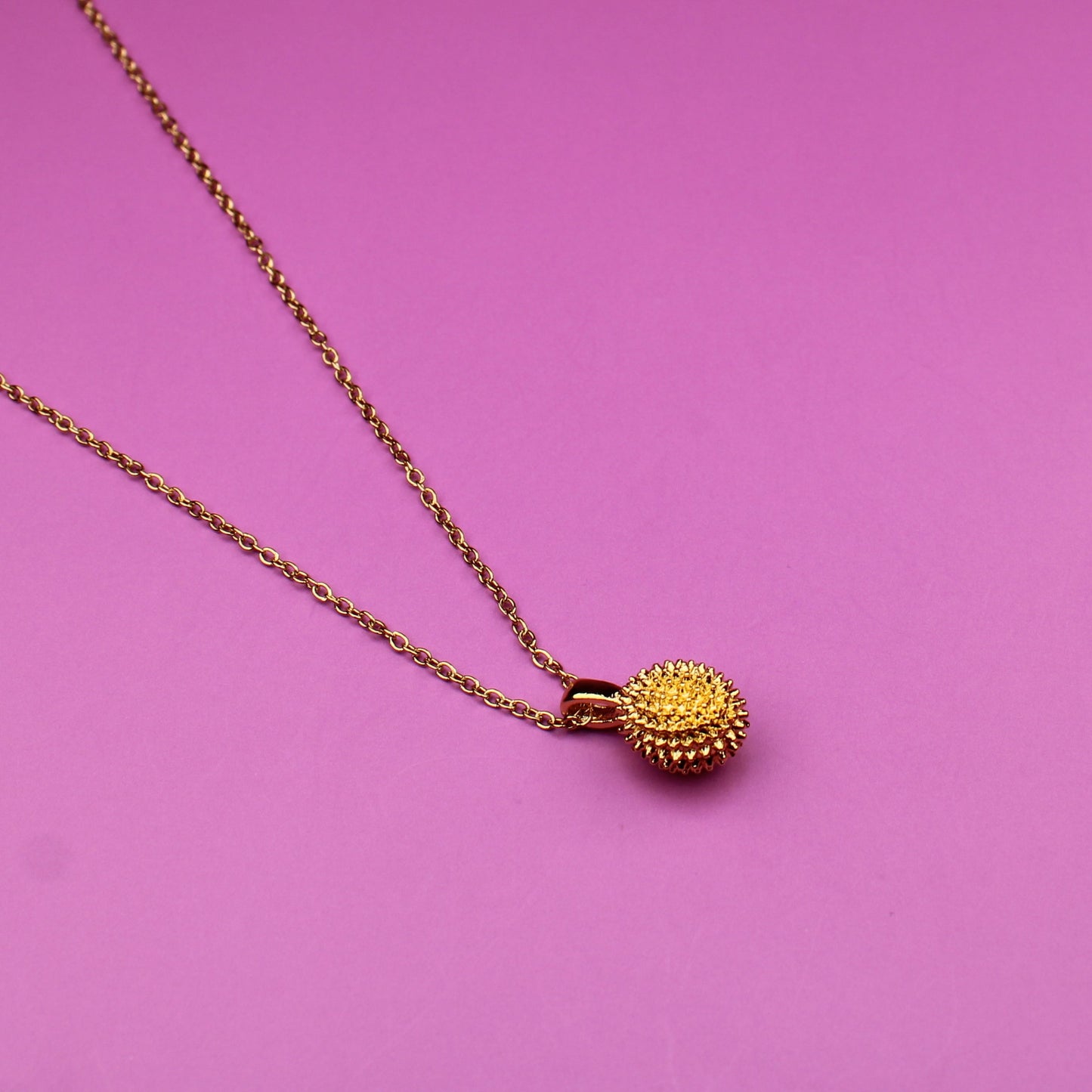 Gold necklace with a pendant on a pink background