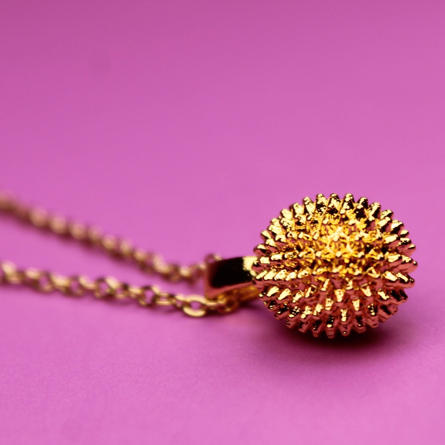 Gold necklace with a textured pendant on a pink background