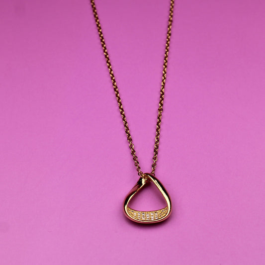 Gold necklace with a heart-shaped pendant on a pink background