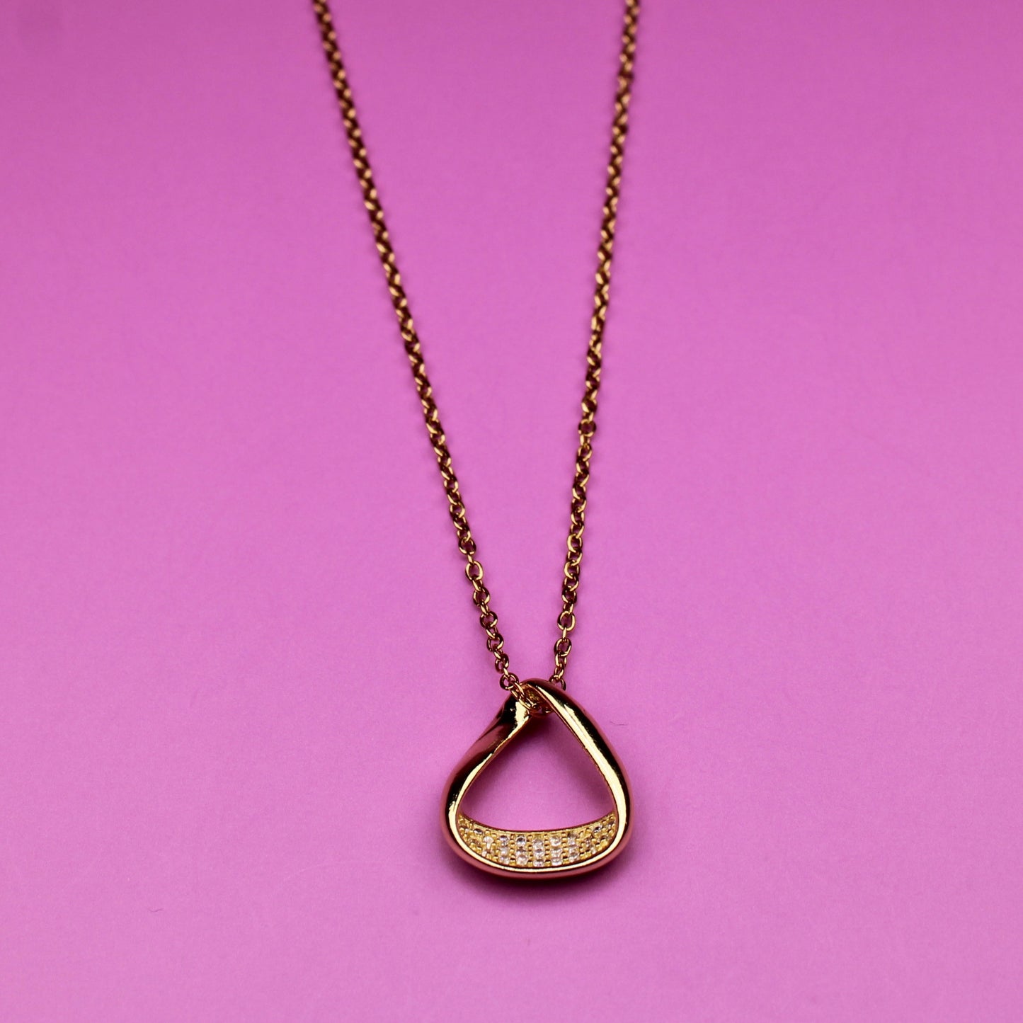 Gold necklace with a heart-shaped pendant on a pink background