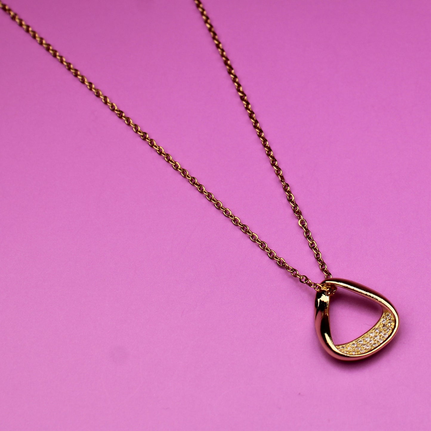 Gold necklace with a heart-shaped pendant on a pink background