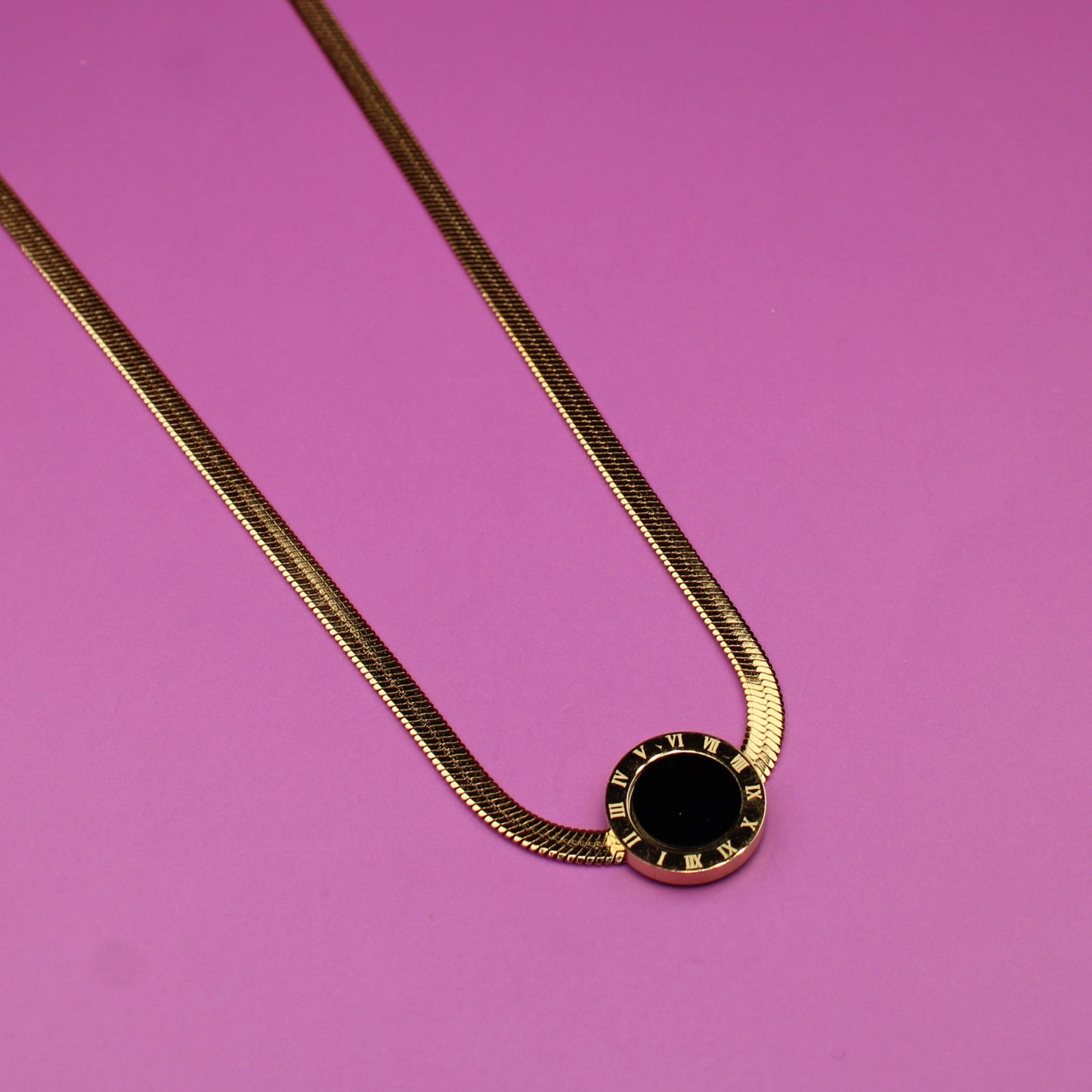 Gold necklace with a black pendant on a pink background