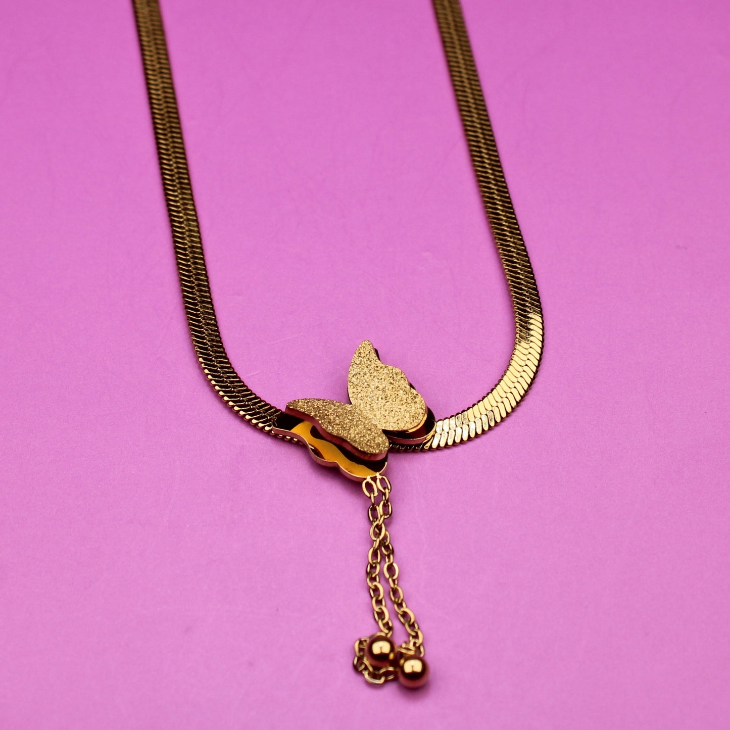 Gold necklace with a butterfly pendant on a pink background
