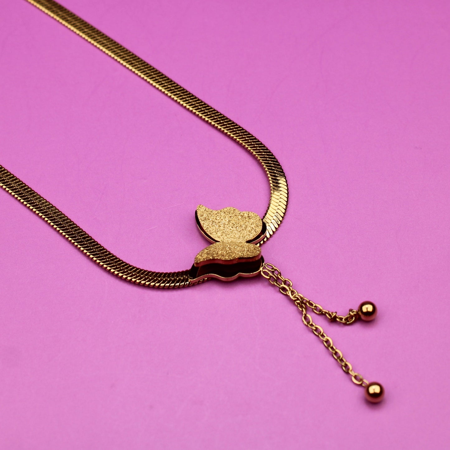Gold necklace with a leaf pendant on a pink background