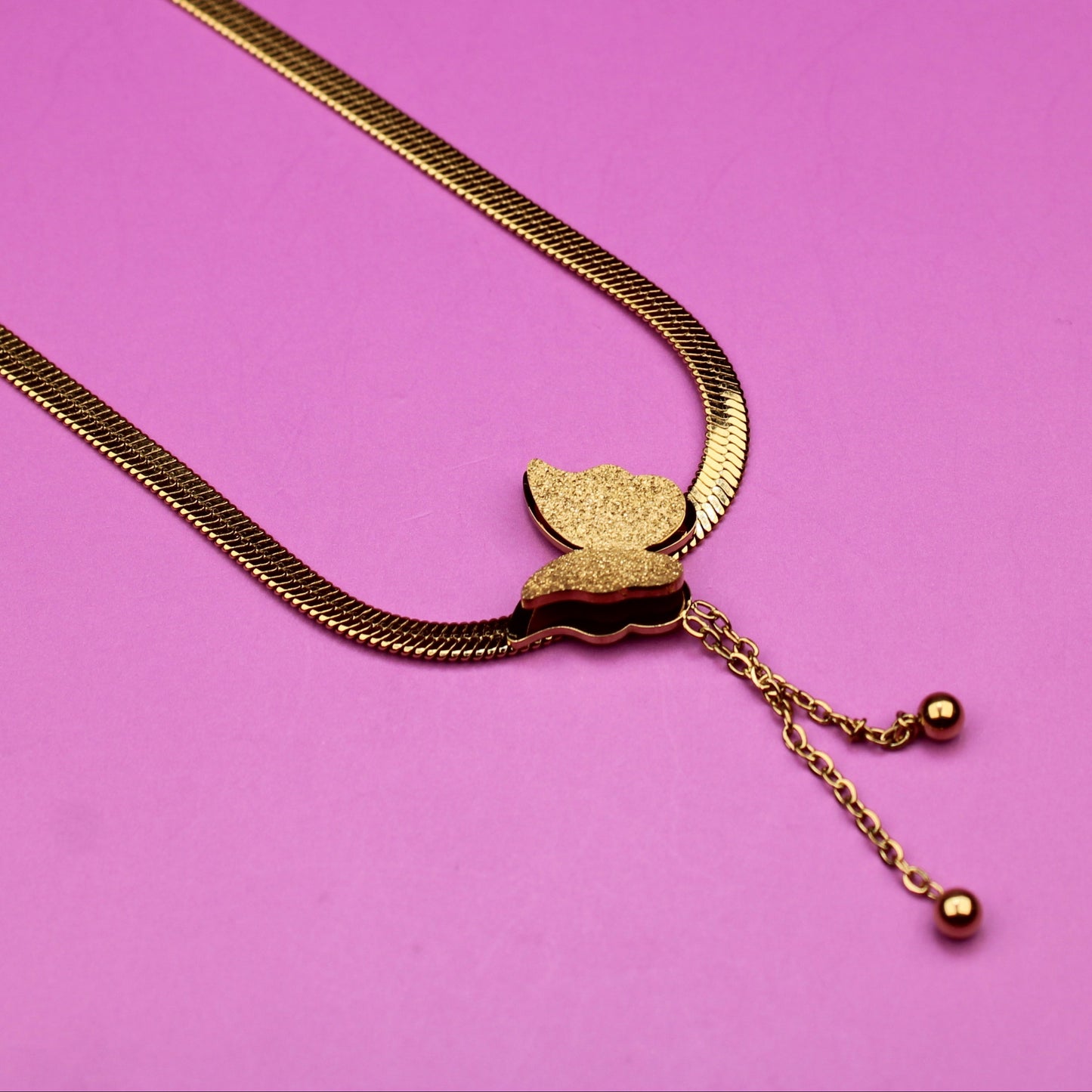 Gold necklace with a leaf pendant on a pink background