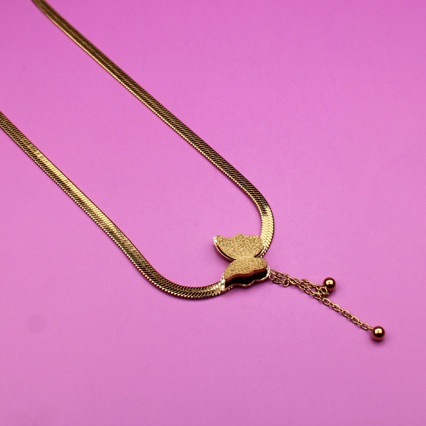 Gold necklace with a heart pendant on a pink background