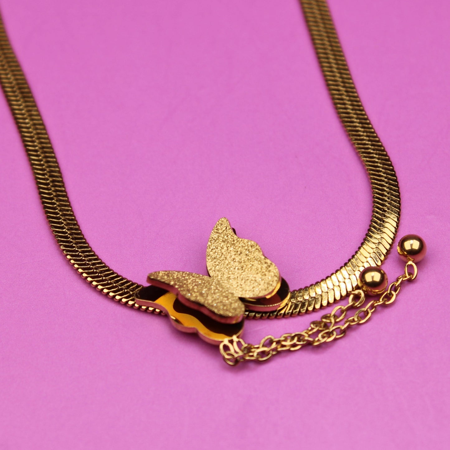 Gold necklace with a butterfly pendant on a pink background