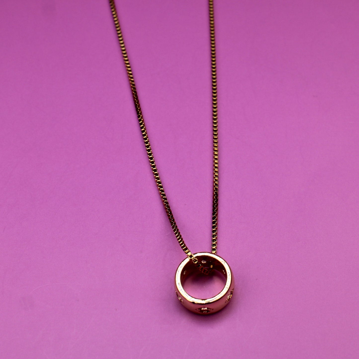 Gold necklace with a circular pendant on a pink background