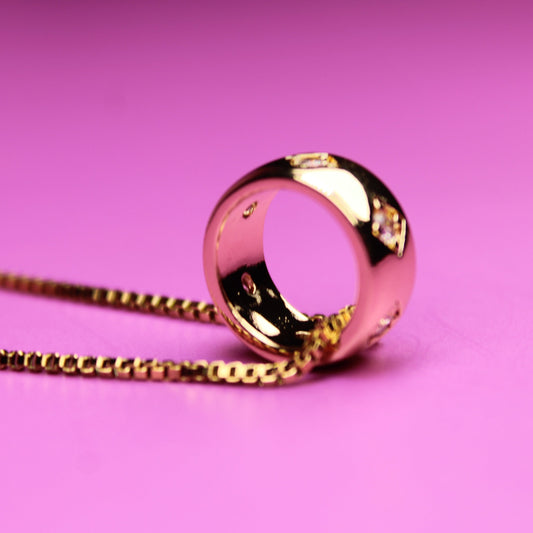 Gold necklace with a ring pendant on a pink background