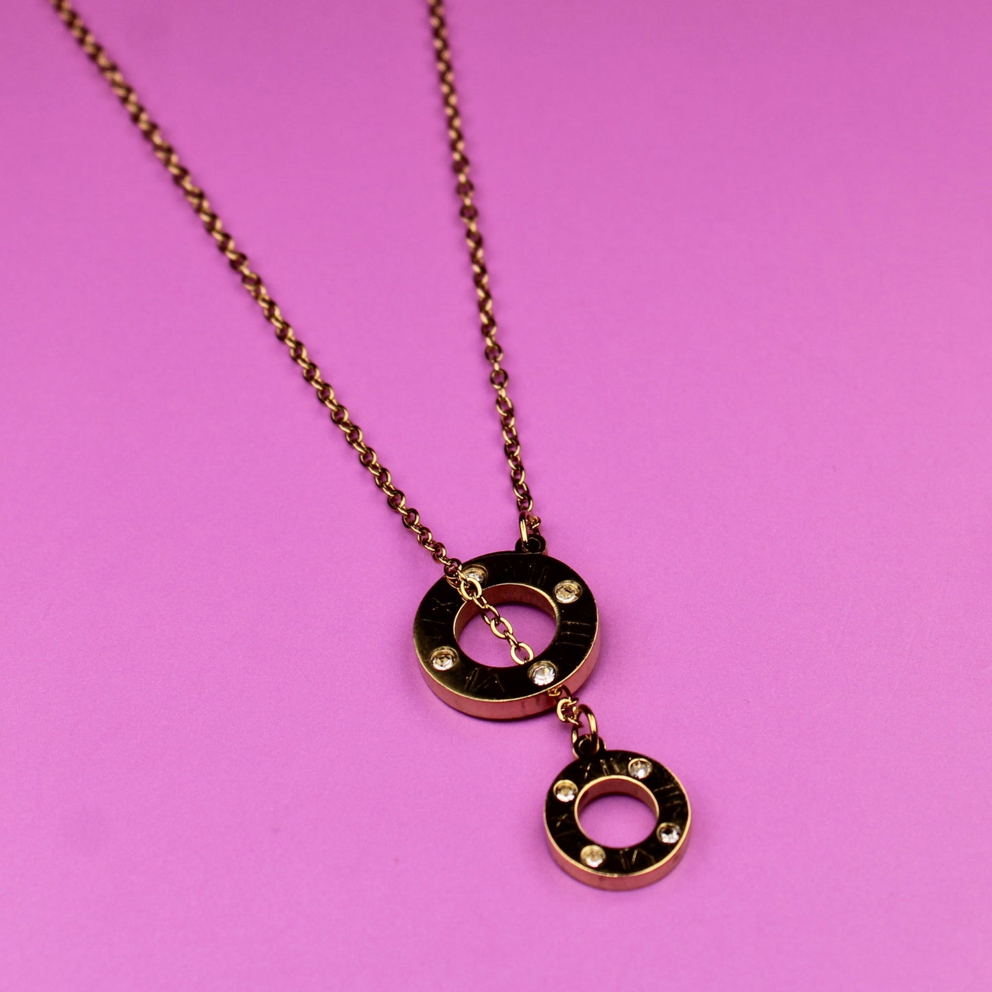 Gold necklace with circular pendants on a pink background