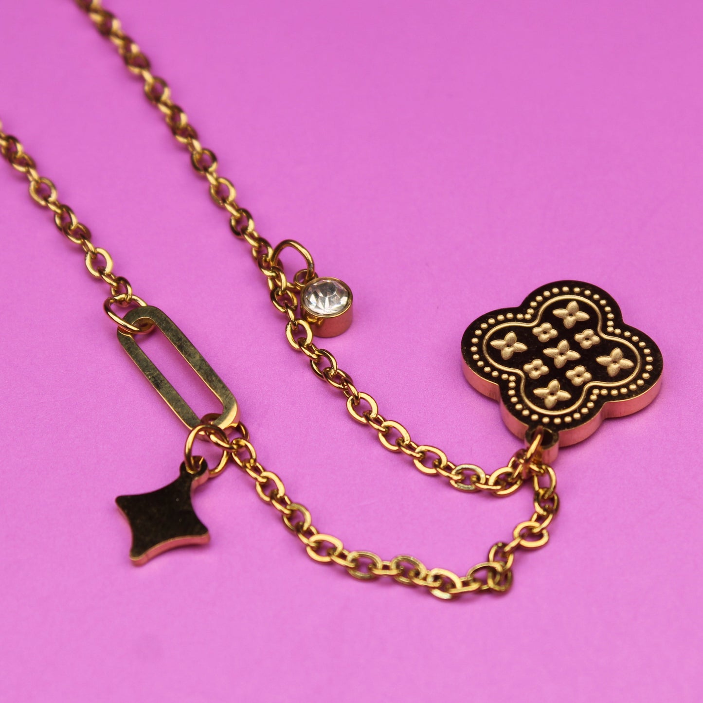 Gold necklace with charms on a pink background