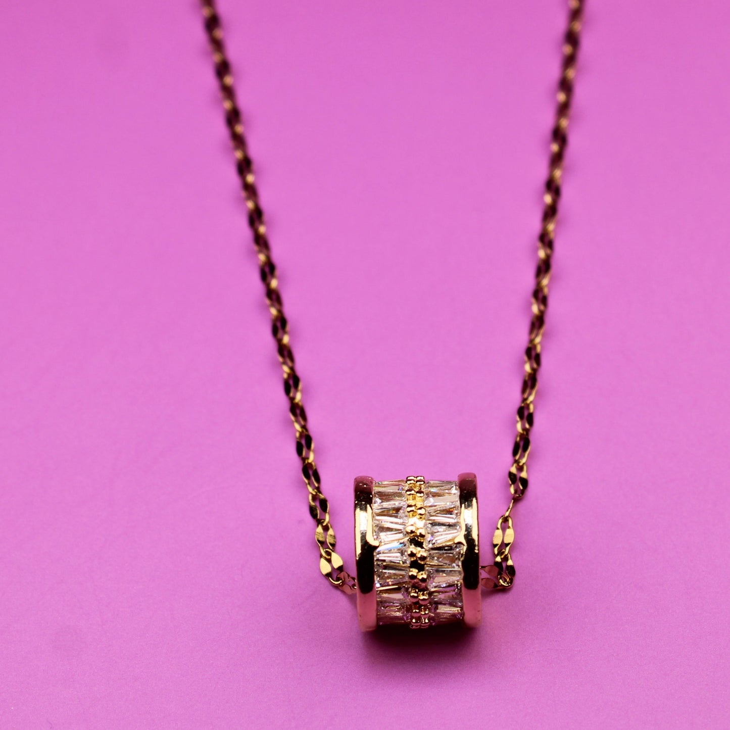 Gold necklace with a textured pendant on a pink background