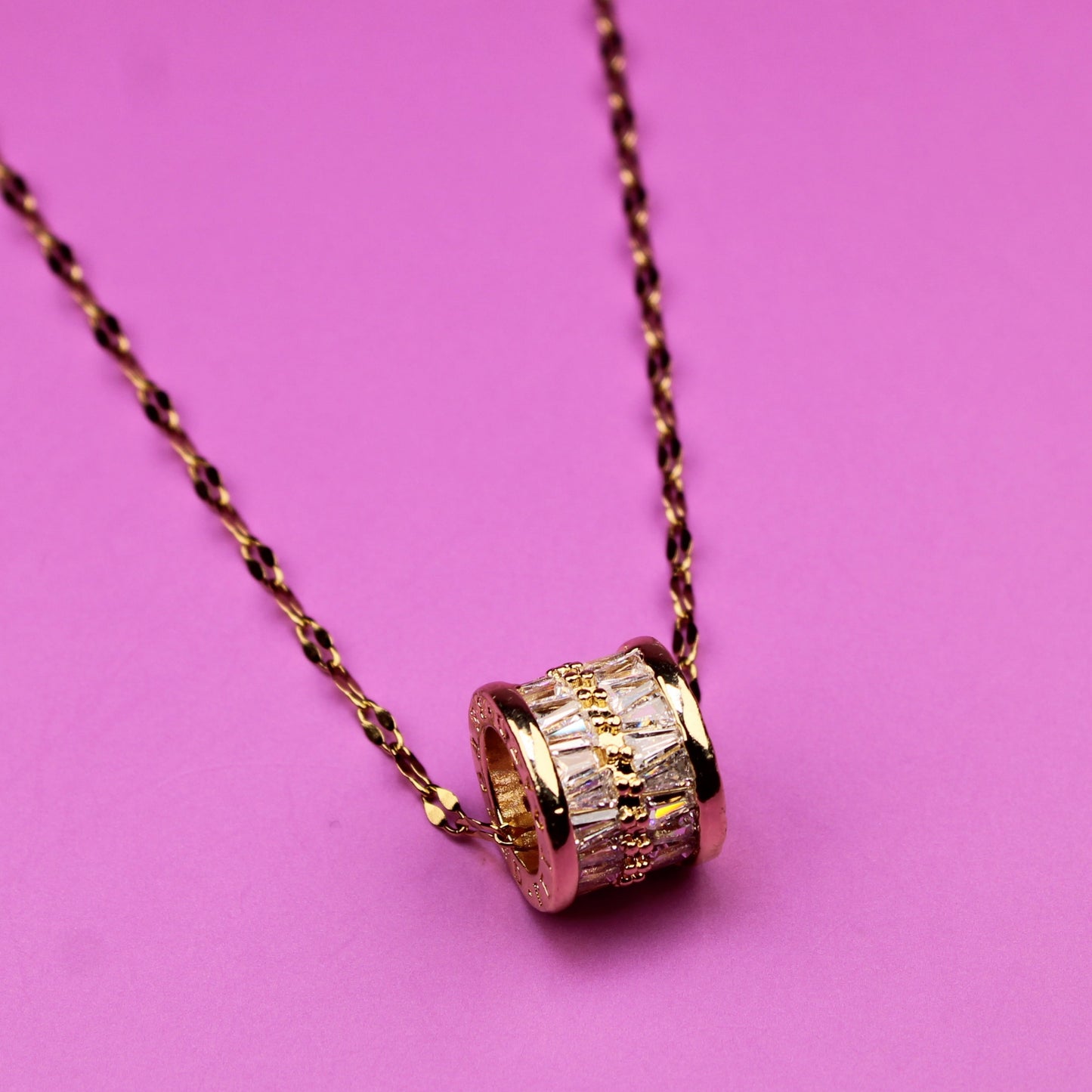 Gold necklace with a cylindrical pendant on a pink background