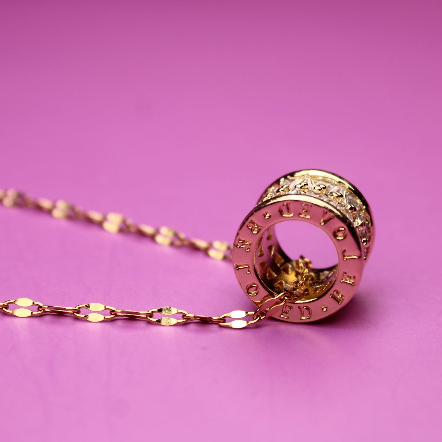 Gold necklace with a circular pendant on a pink background