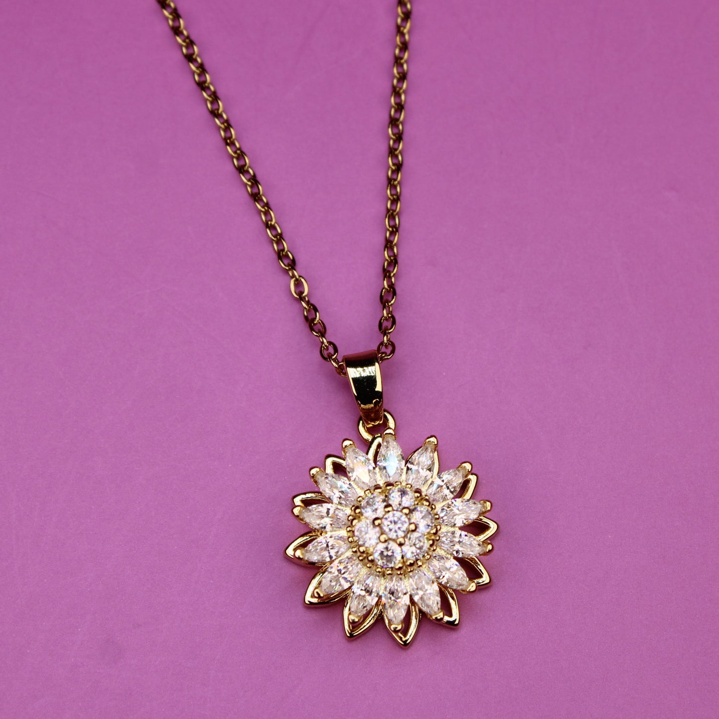 Gold necklace with a sunflower-shaped pendant on a purple background