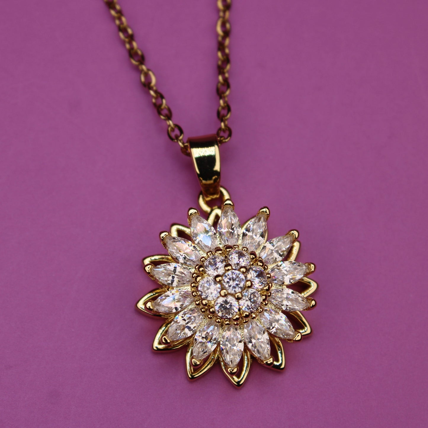 Gold necklace with a sunflower-shaped pendant on a purple background