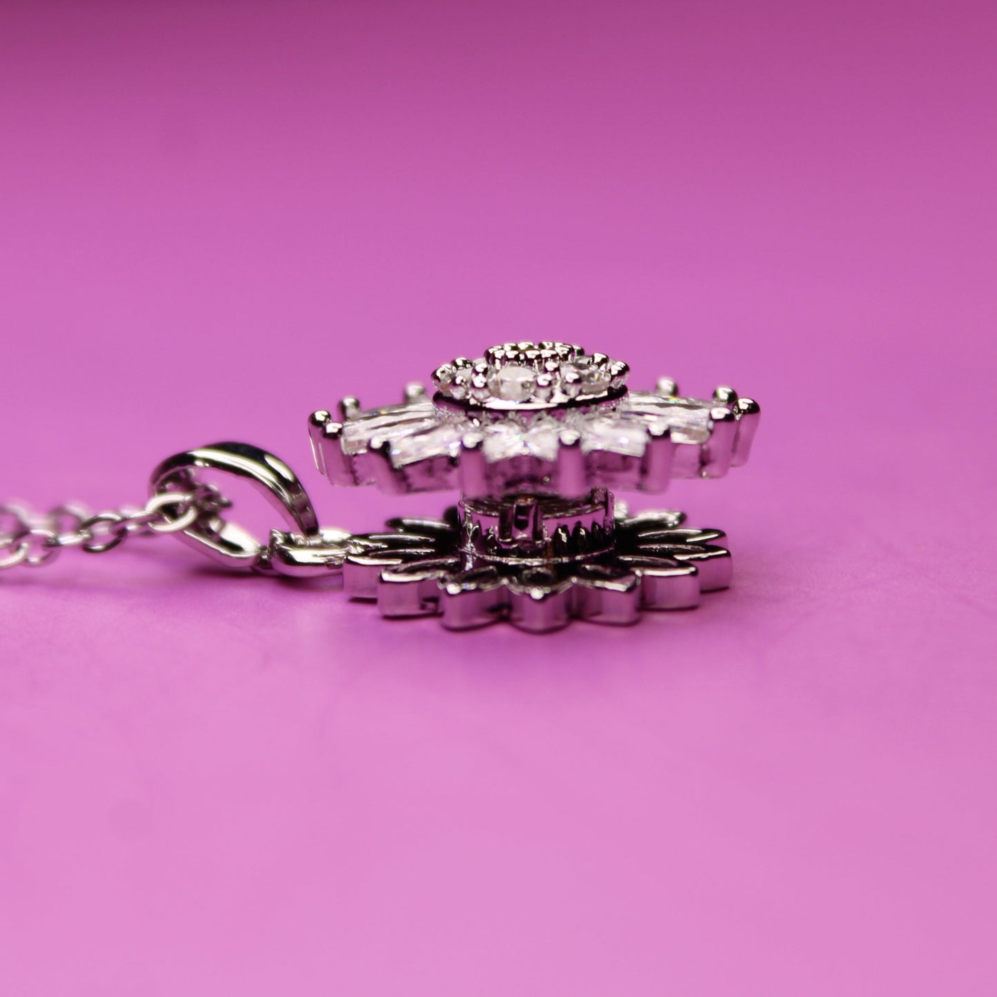 Silver necklace with a floral pendant on a pink background