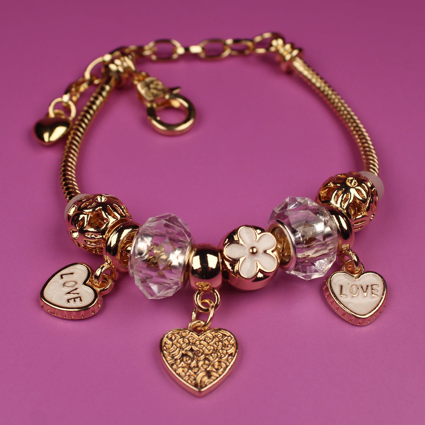 Gold bracelet with heart-shaped charms on a pink background