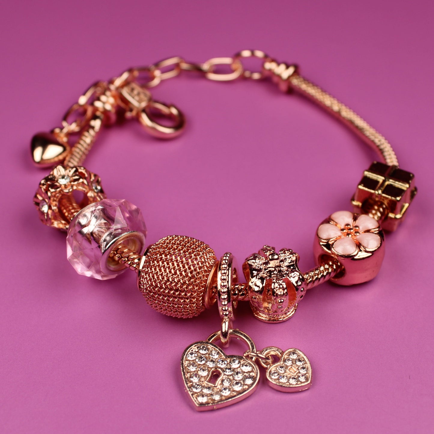 Rose gold bracelet with charms on a pink background