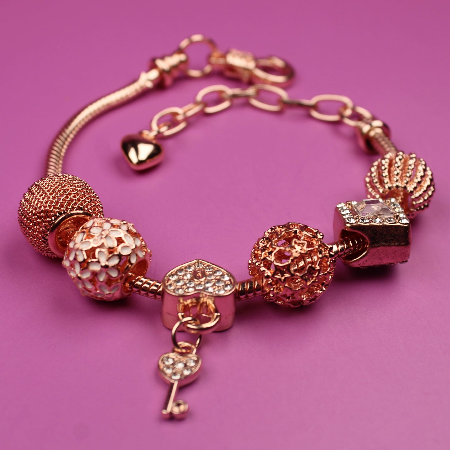 Rose gold bracelet with various charms on a pink background