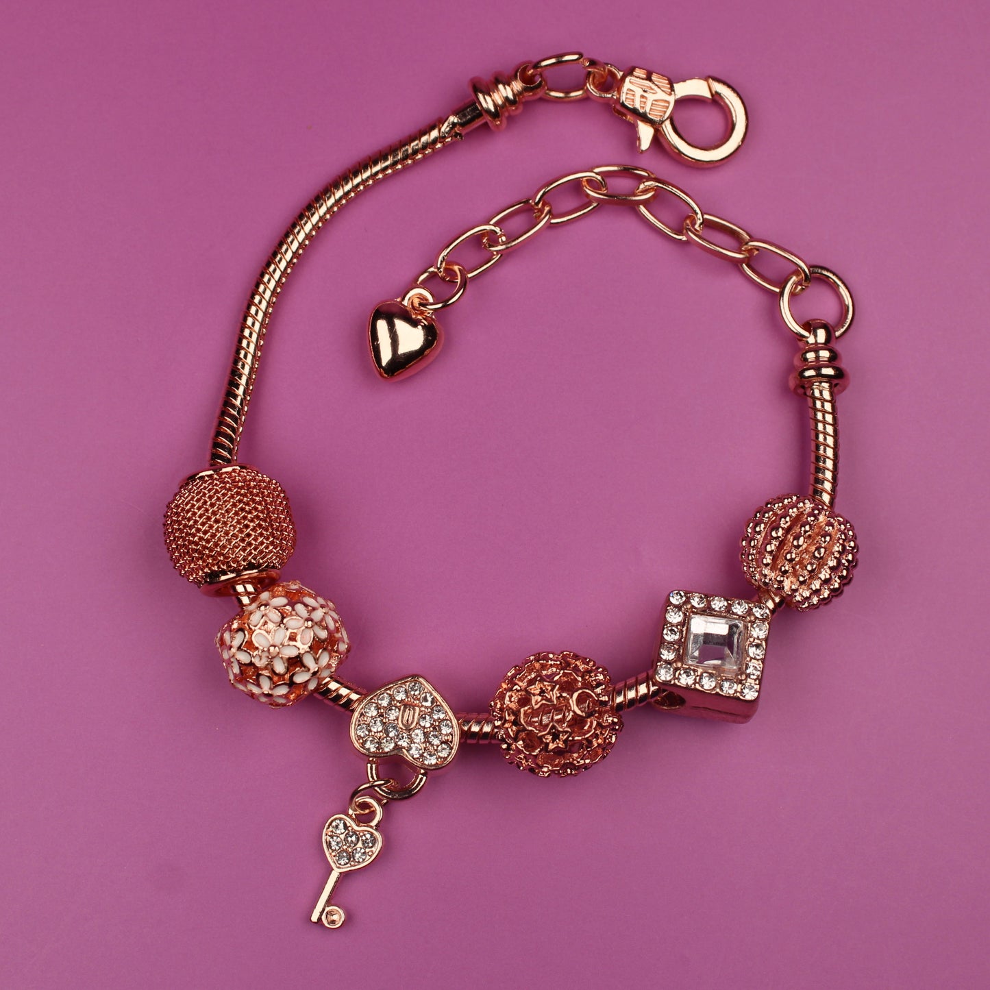 Gold bracelet with various charms on a pink background