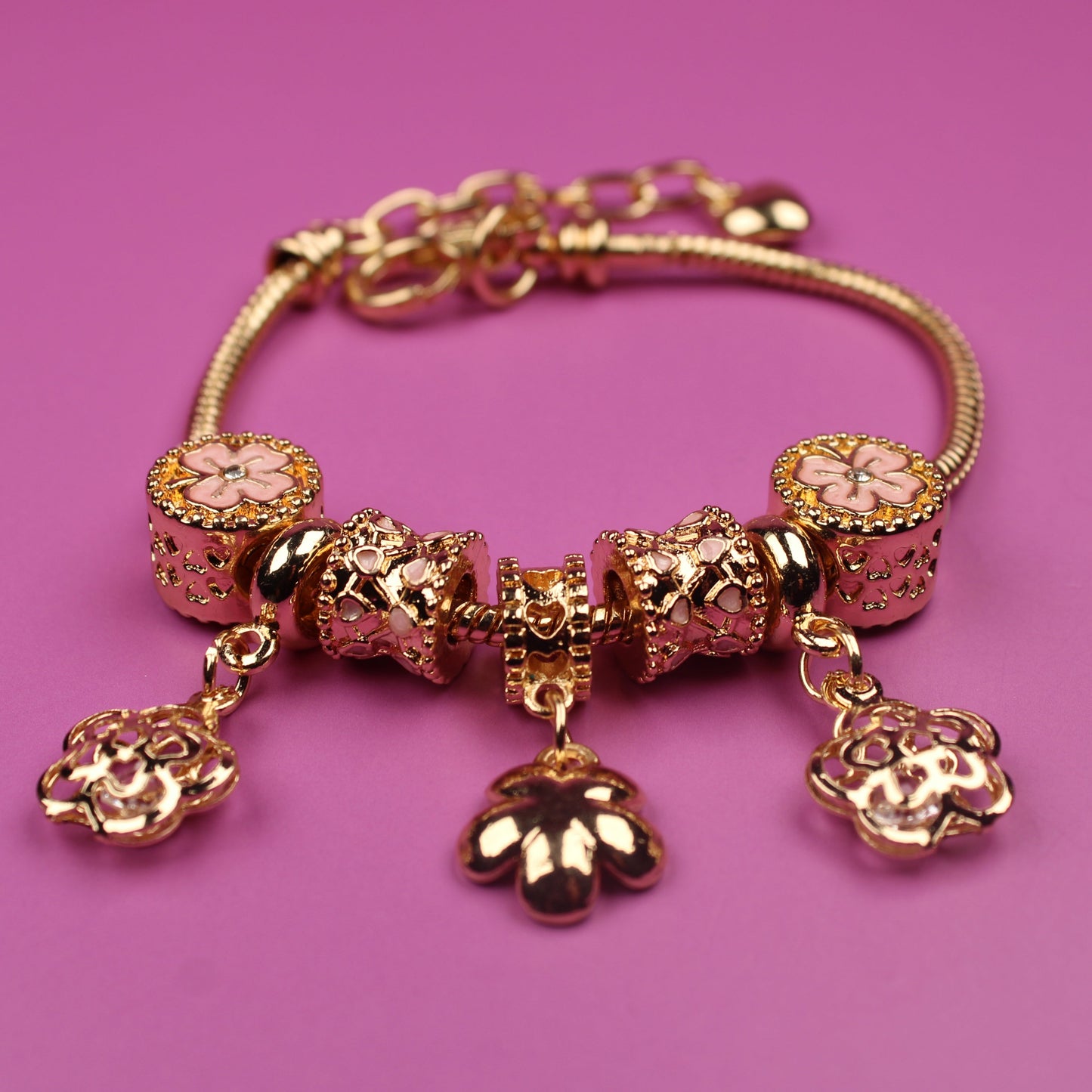 Gold bracelet with charms on a pink background