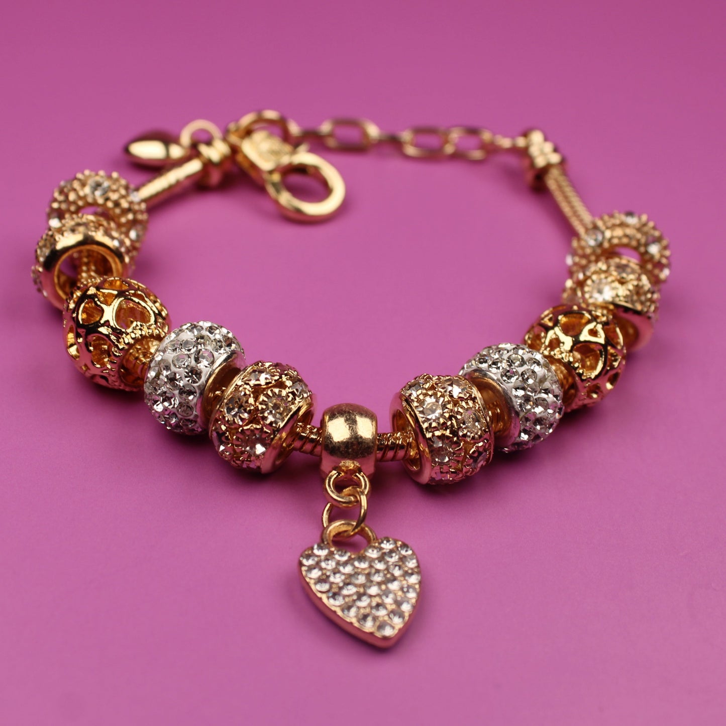 Gold bracelet with heart charm on a pink background