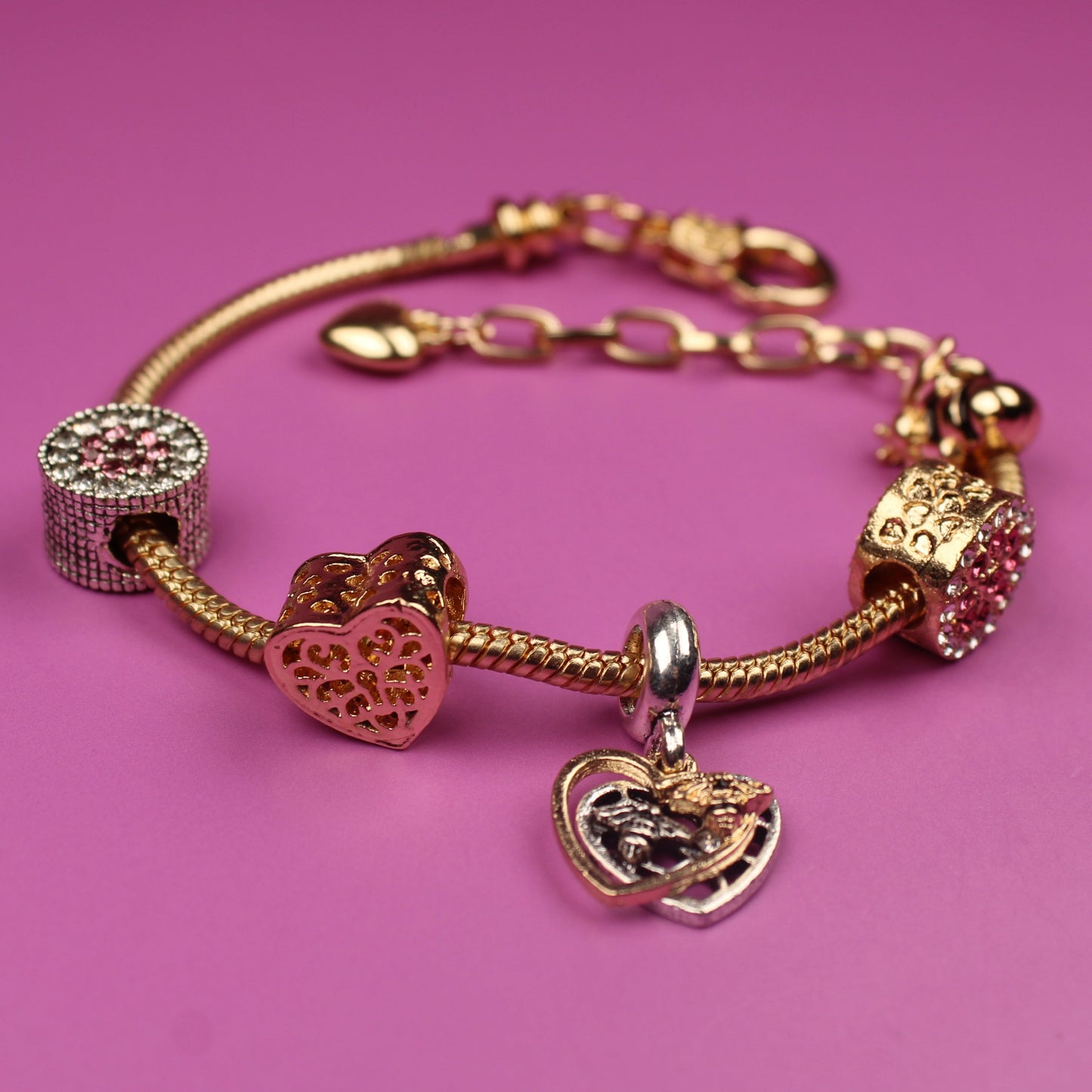 Gold bracelet with heart-shaped charms on a pink background