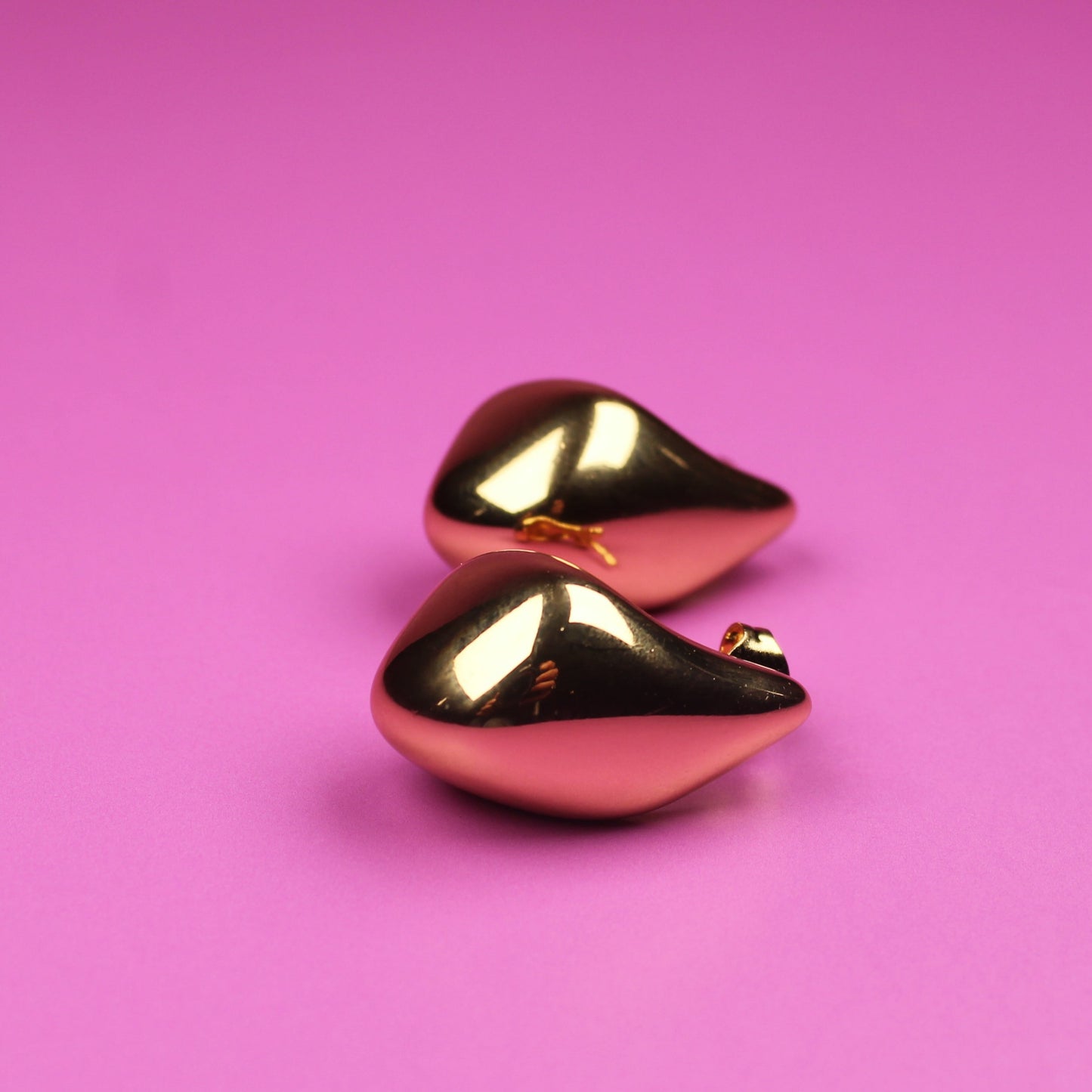 Gold teardrop-shaped earrings on a pink background