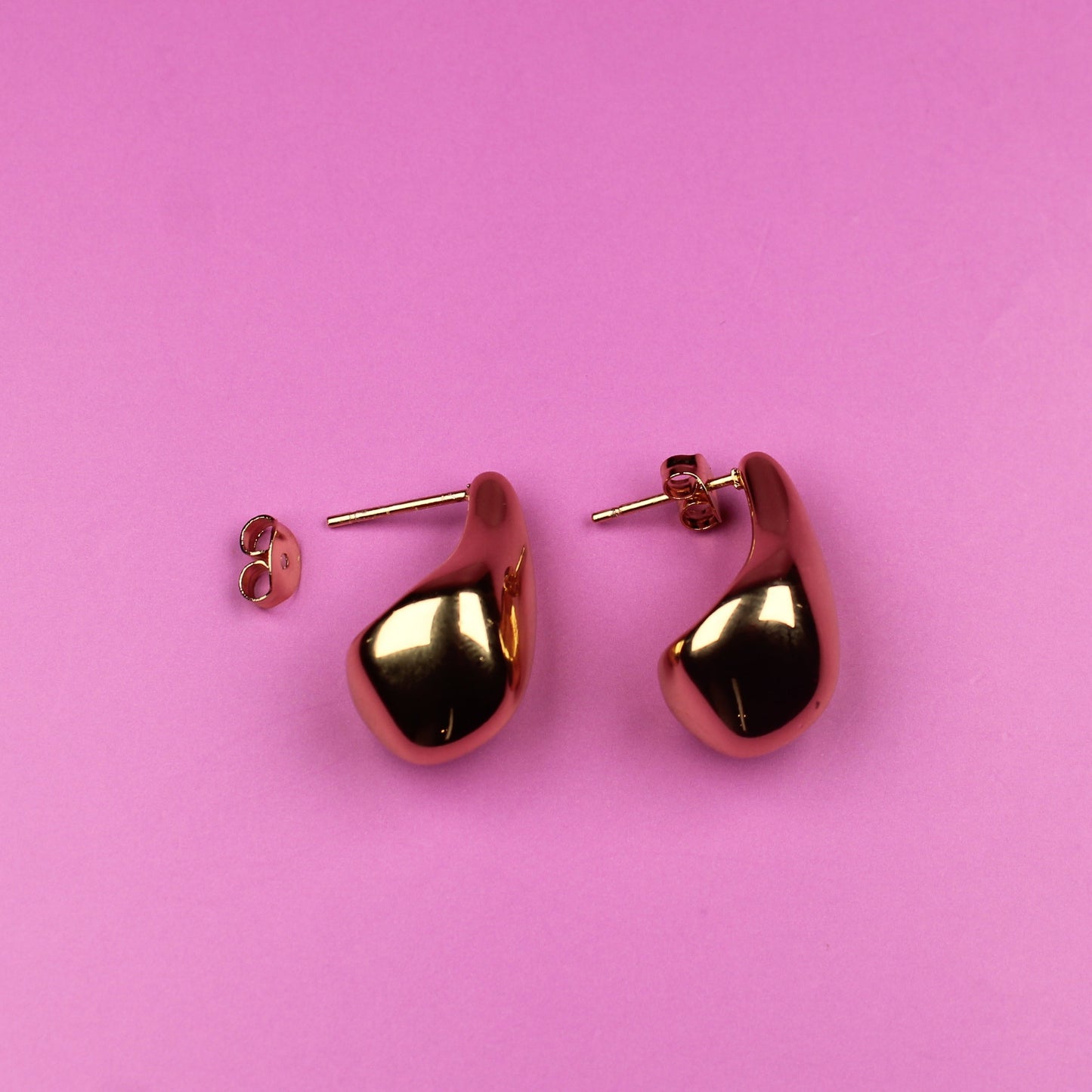 Gold heart-shaped earrings on a pink background