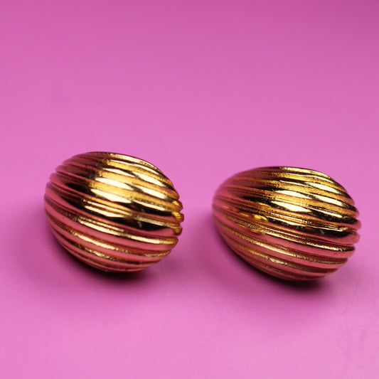 Gold ribbed earrings on a pink background