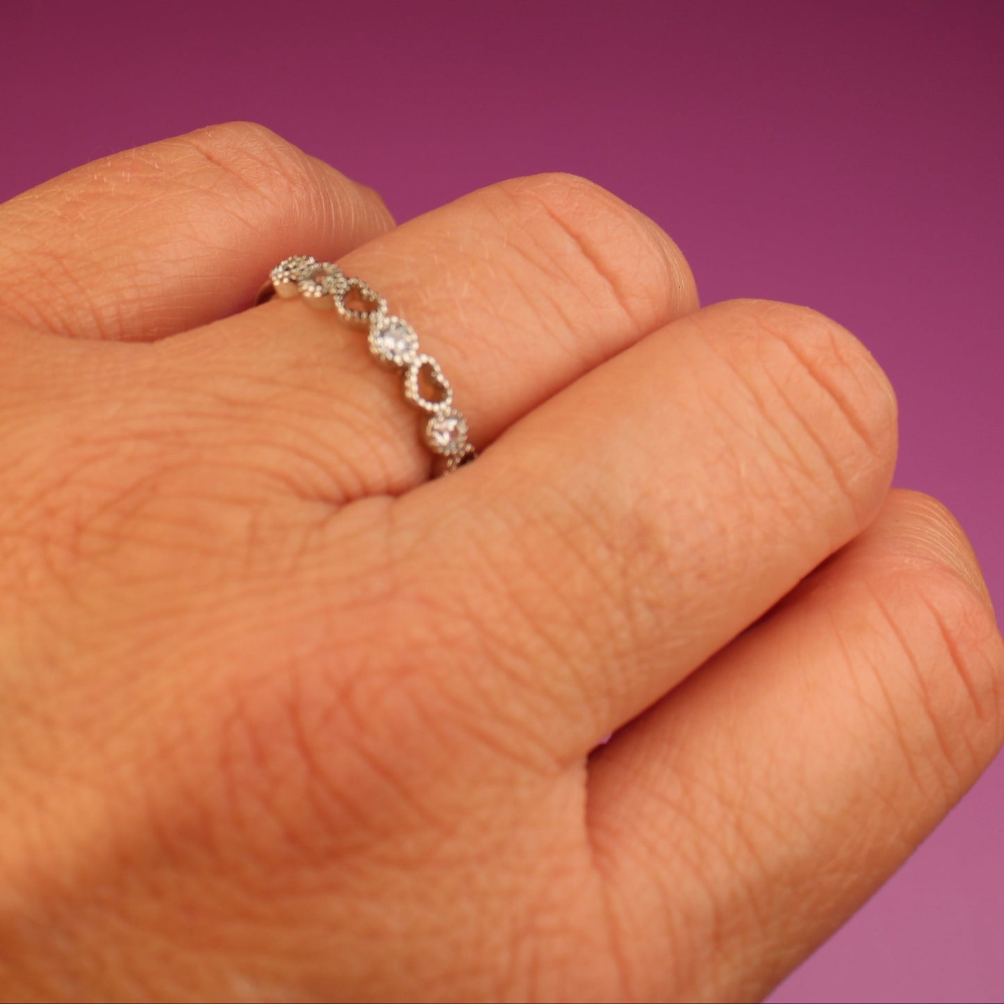 Hand wearing a silver ring on a purple background