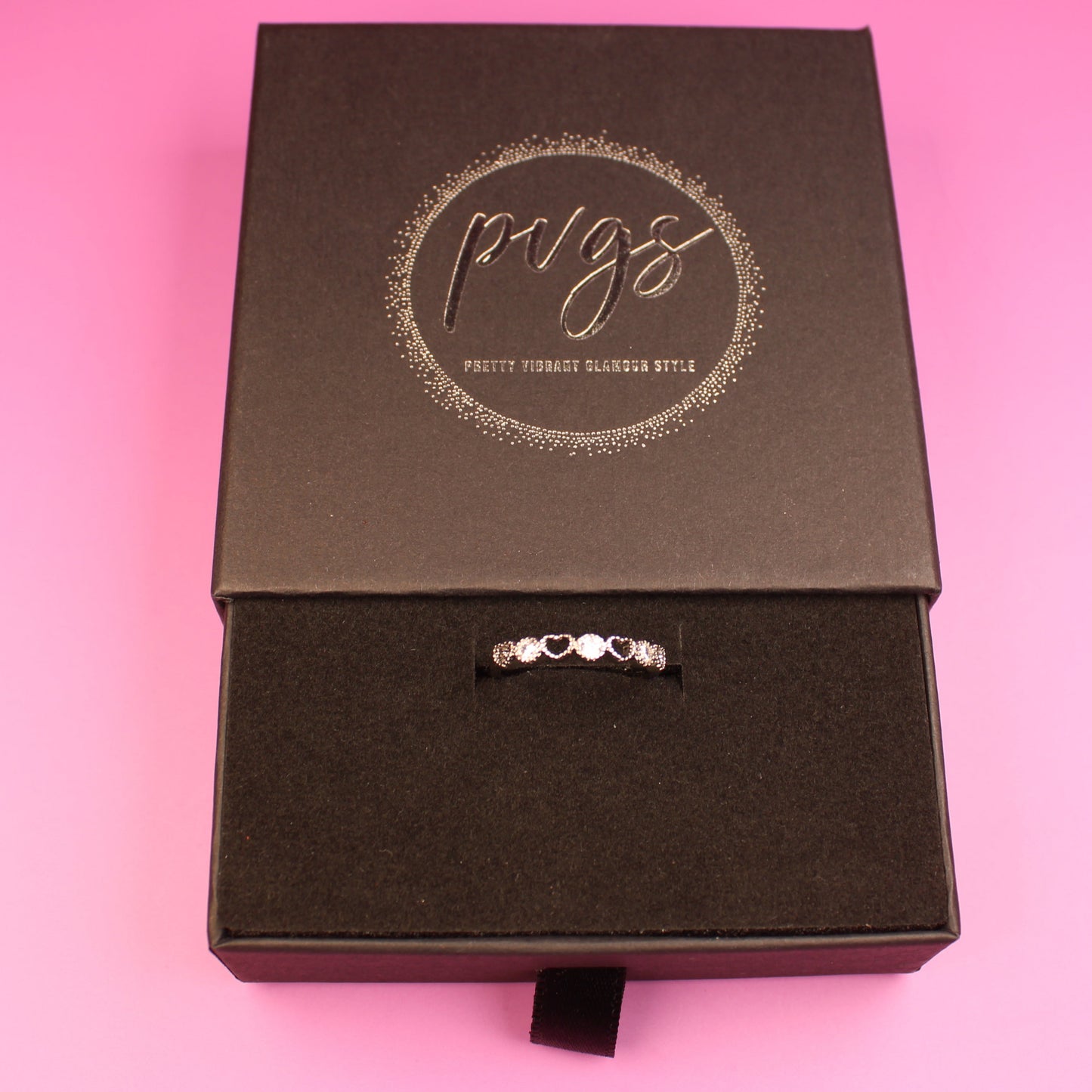 Black jewelry box with a ring on a pink background