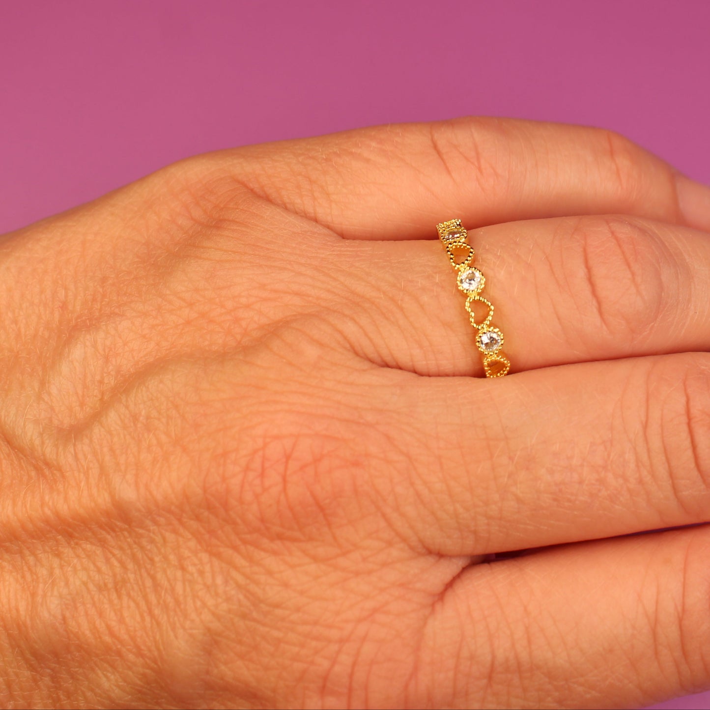 Hand wearing a gold ring with small stones on a pink background