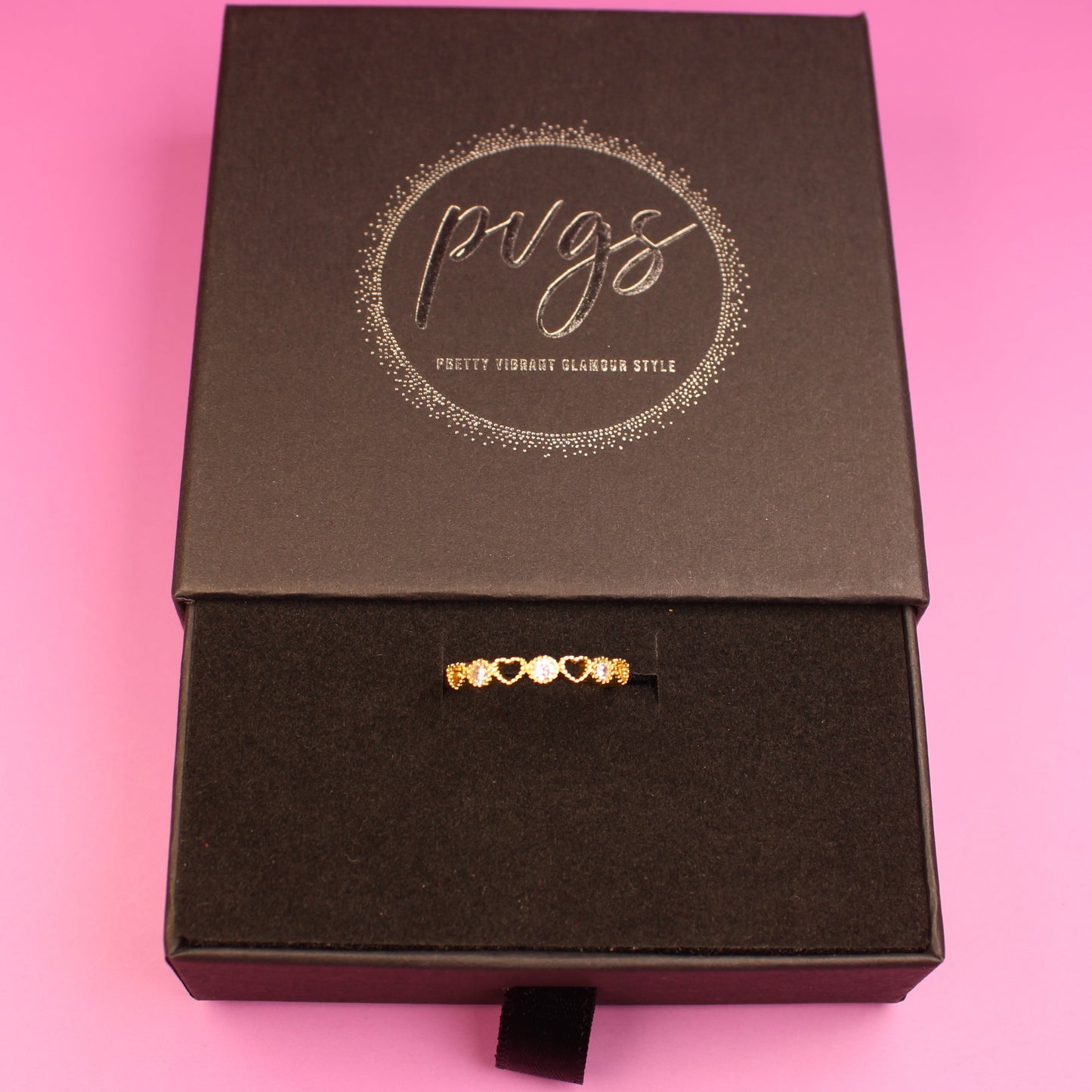 Black jewelry box with a gold necklace on a pink background