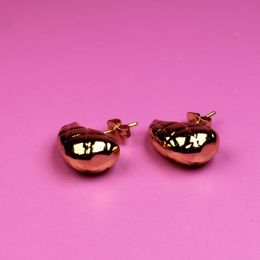Rose gold cat-shaped earrings on a pink background