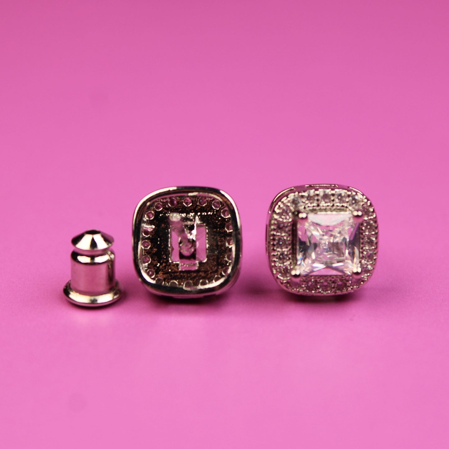Two diamond-studded earrings on a pink background
